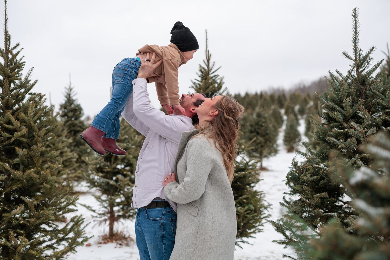 A romantic winter engagement photoshoot among snow-covered evergreen trees at a Christmas tree farm.
