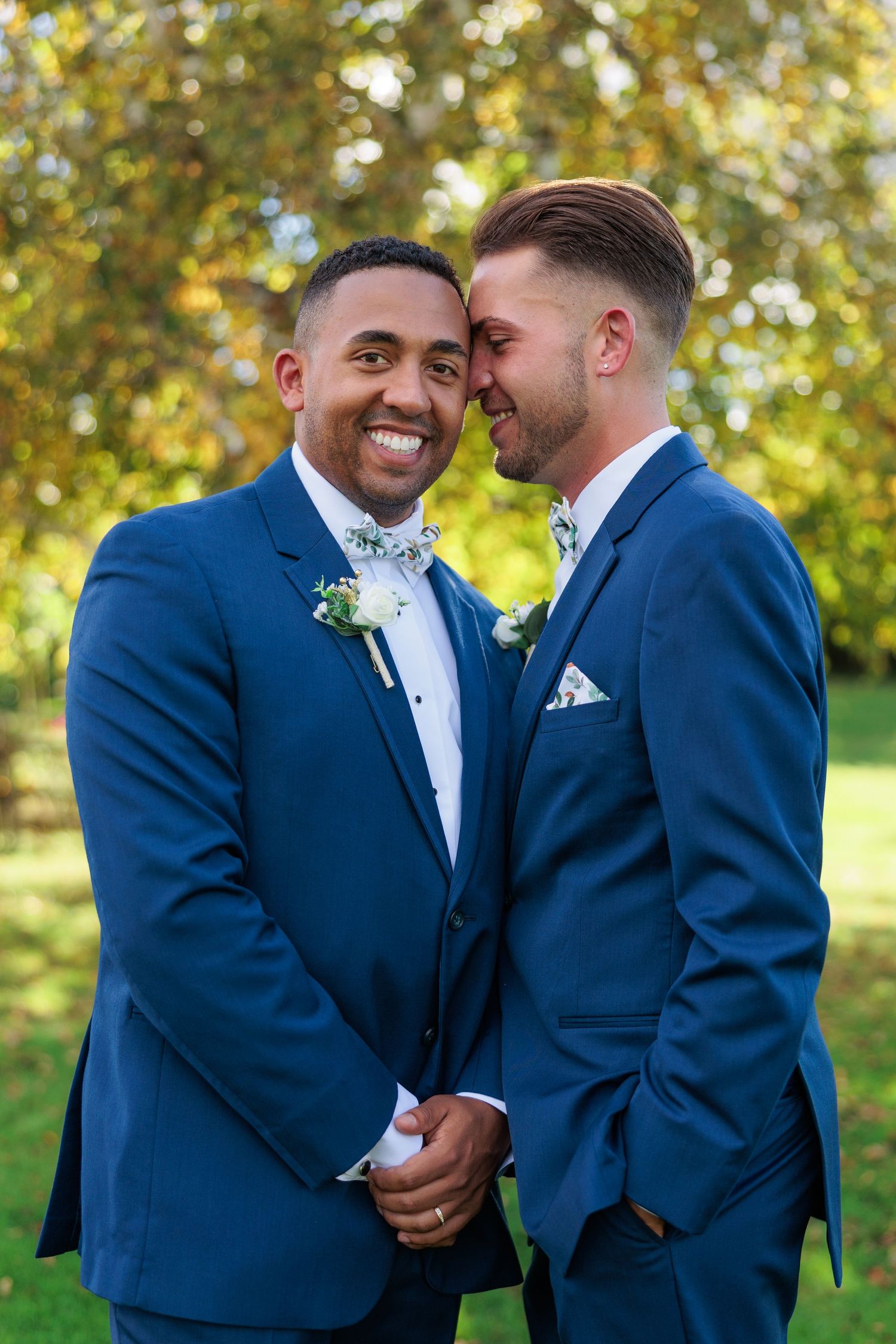 Couple in matching navy suits share joyful moments against autumn foliage background.