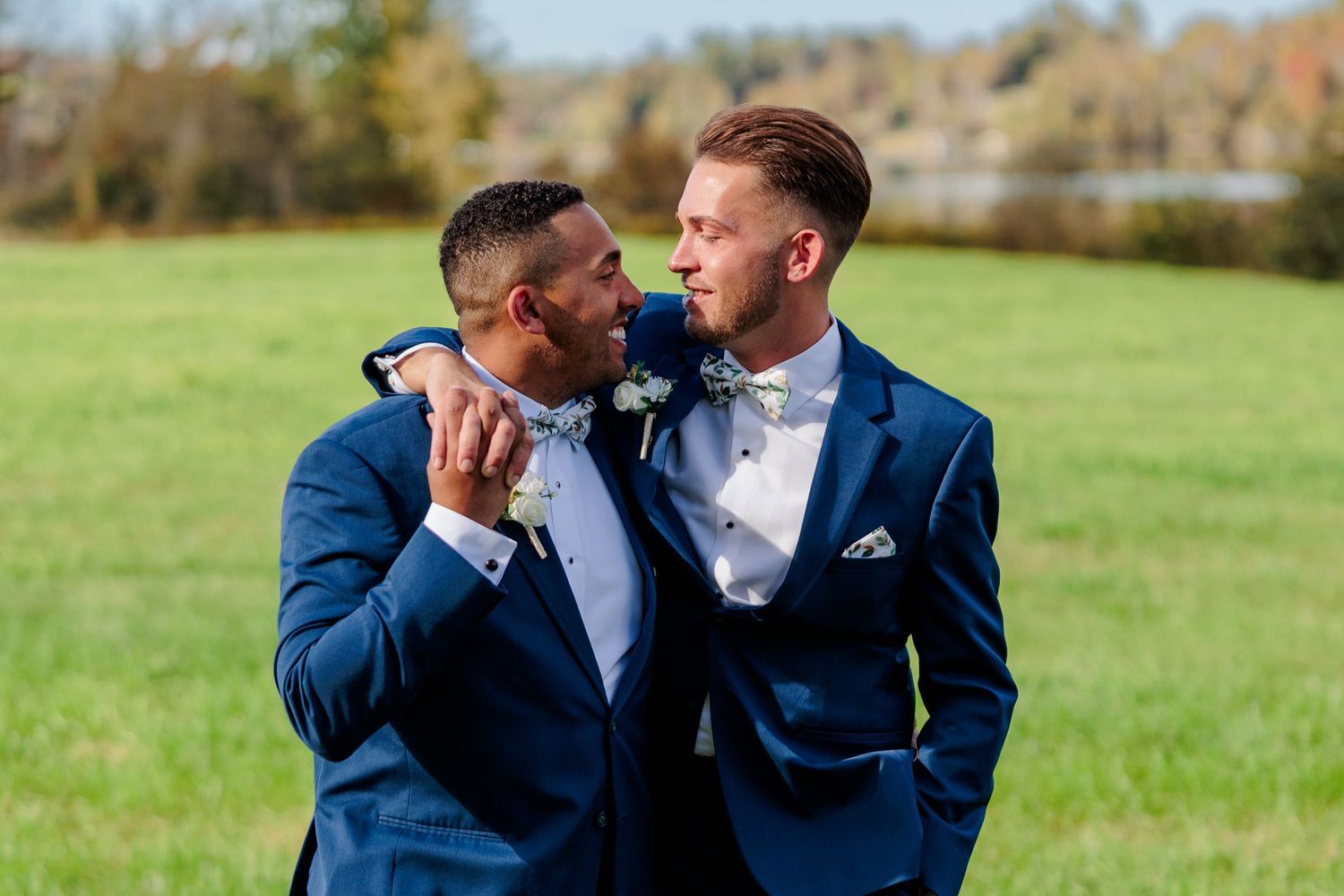 Couple in navy suits share tender moments in sunlit autumn field.