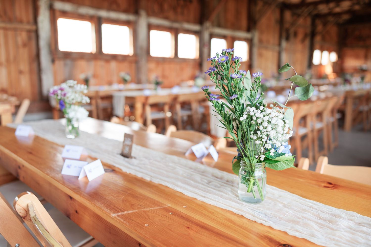 Rustic barn wedding reception tables decorated with wildflower centerpieces in mason jars and lace runners.