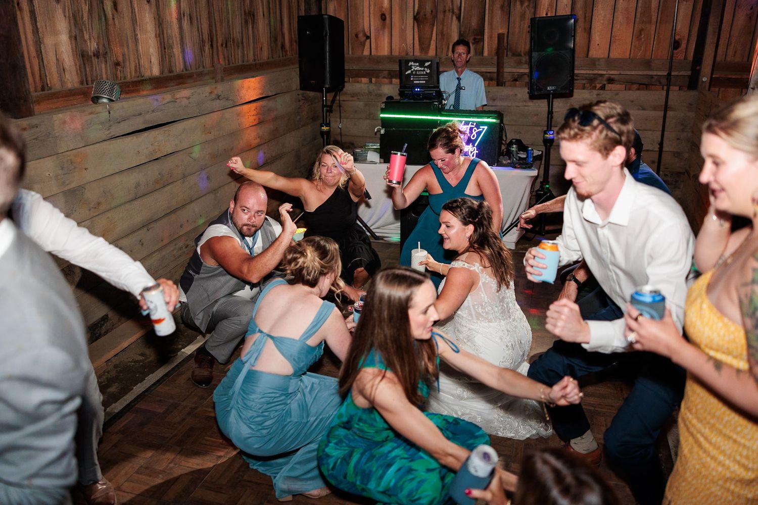 Wedding guests sit and dance on floor together during energetic barn wedding reception celebration.