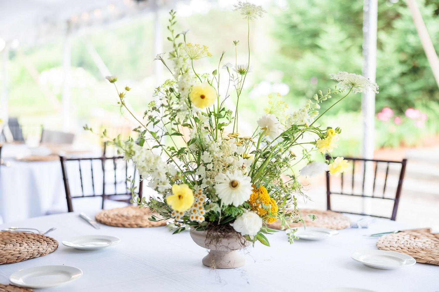 Elegant floral centerpiece with white daisies and yellow flowers in a stone vase on a reception table.