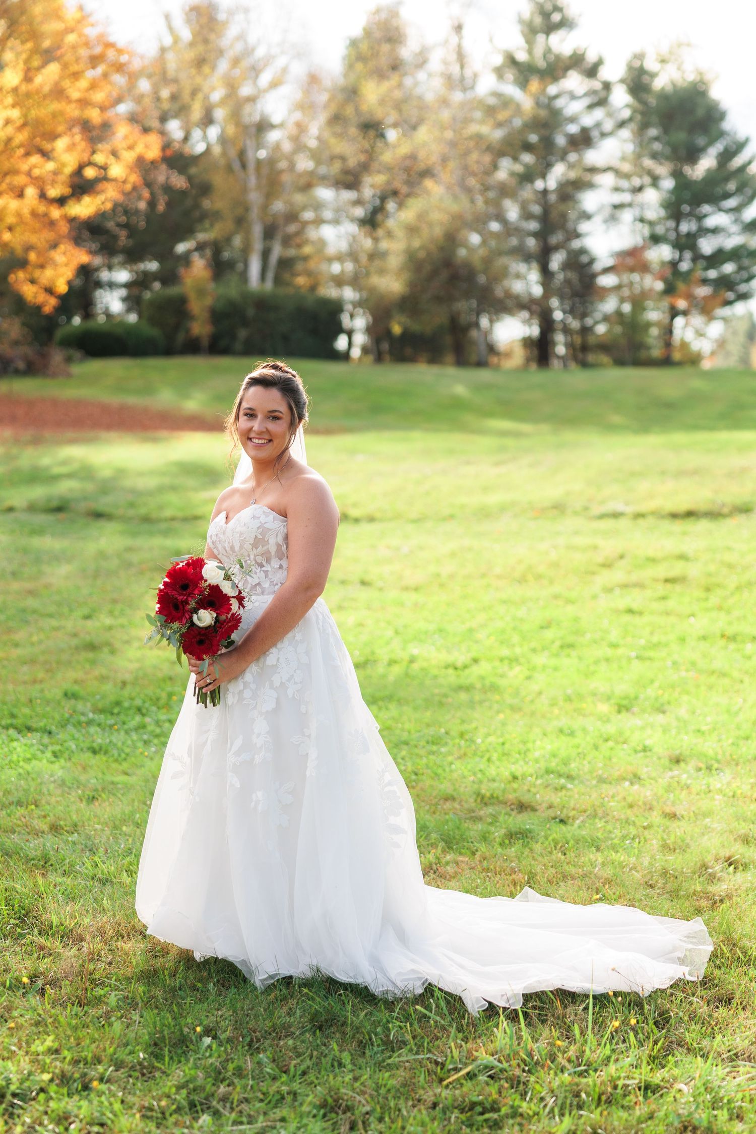 Bride in flowing white gown poses on grassy hill during golden autumn afternoon.