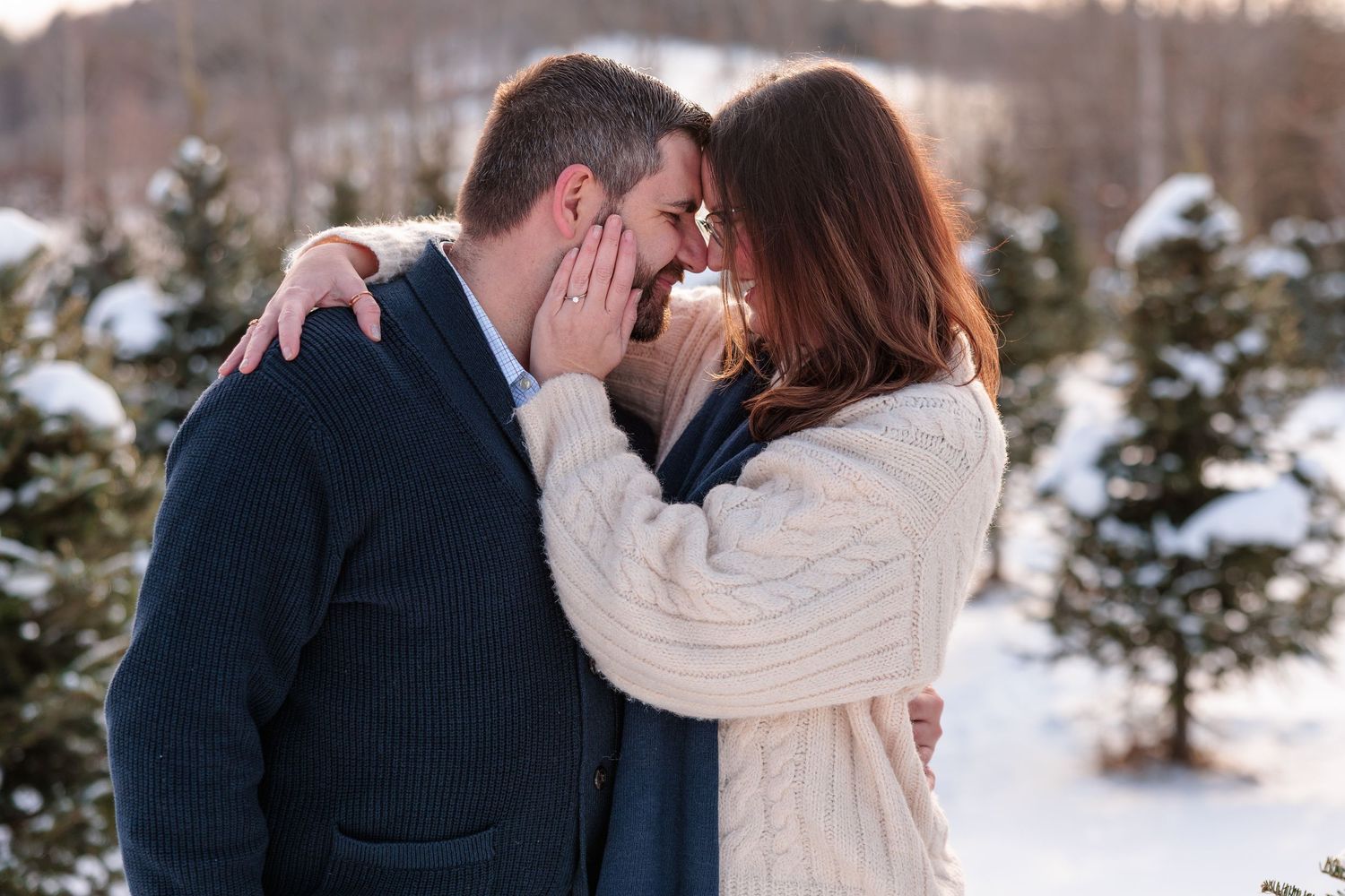 Romantic couple touching foreheads and smiling among snow-covered Christmas trees.
