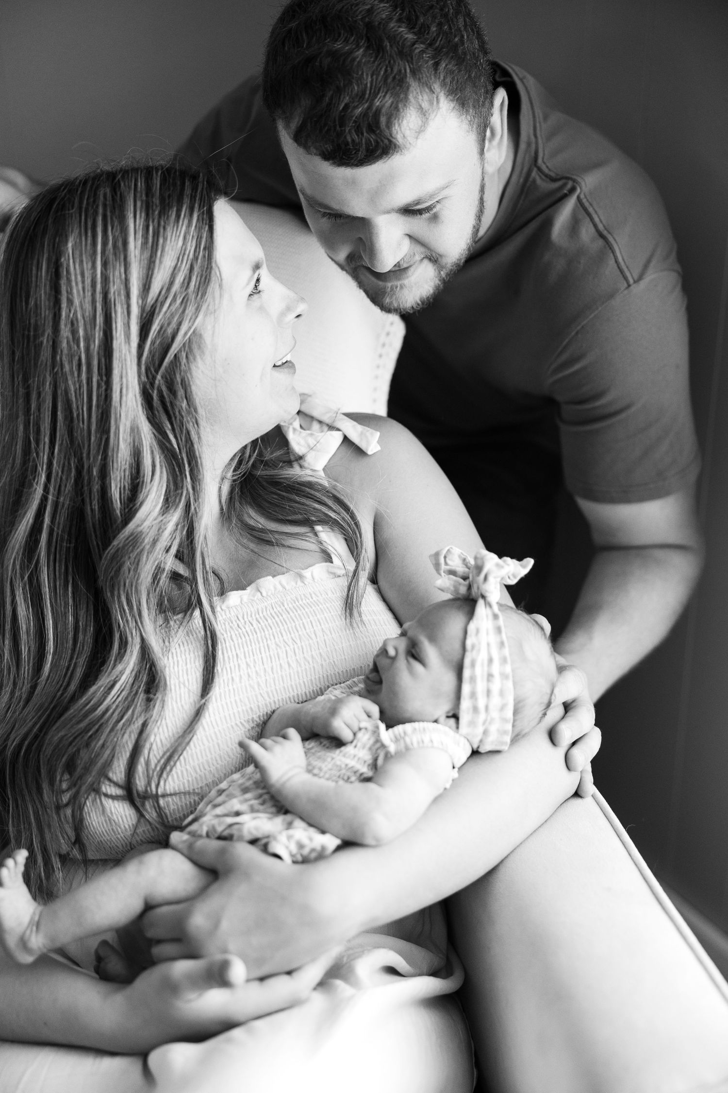 Black and white portrait of parents sharing a tender moment while cradling their newborn.