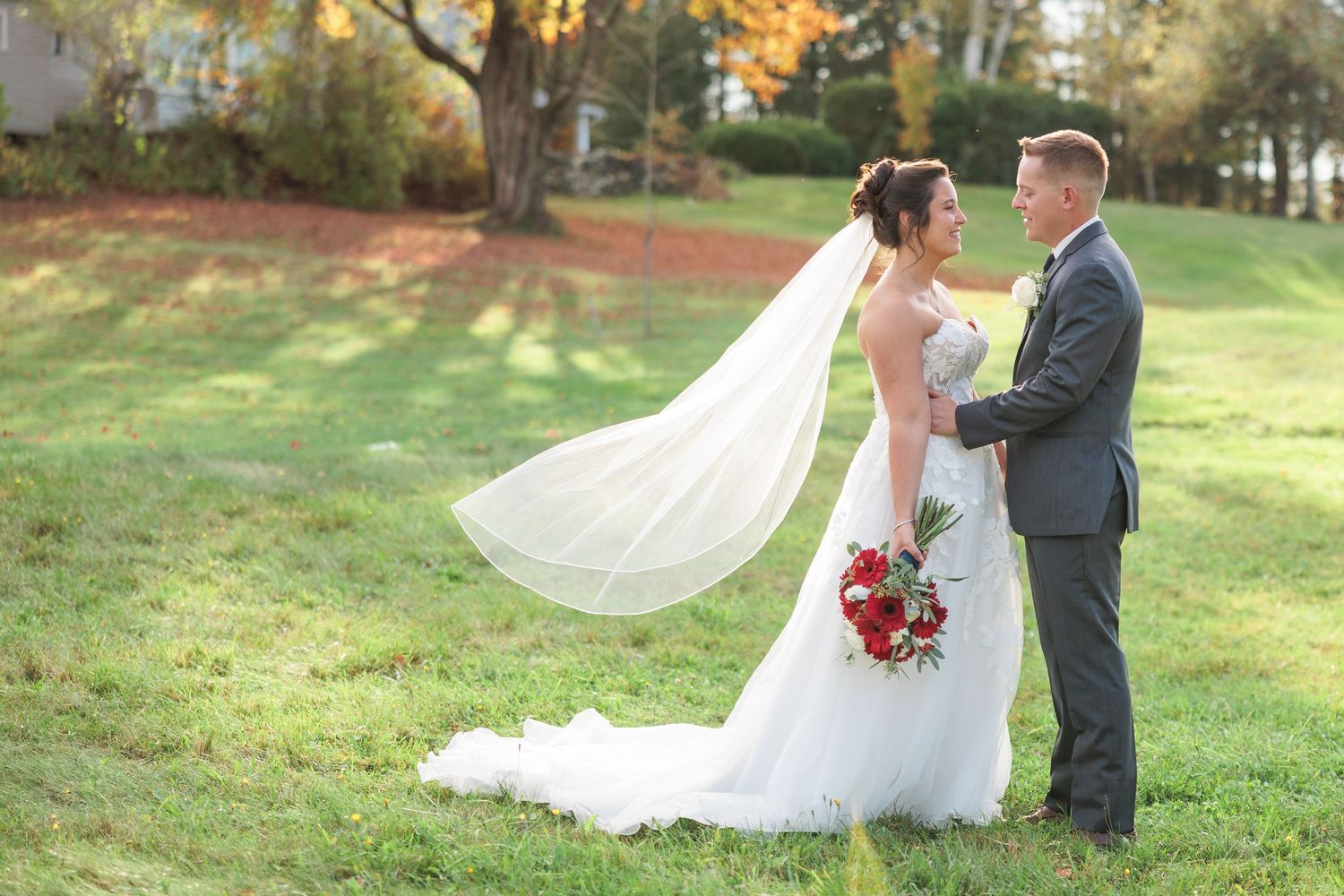 Elegant wedding couple poses in outdoor fall setting with flowing white dress and autumn leaves.