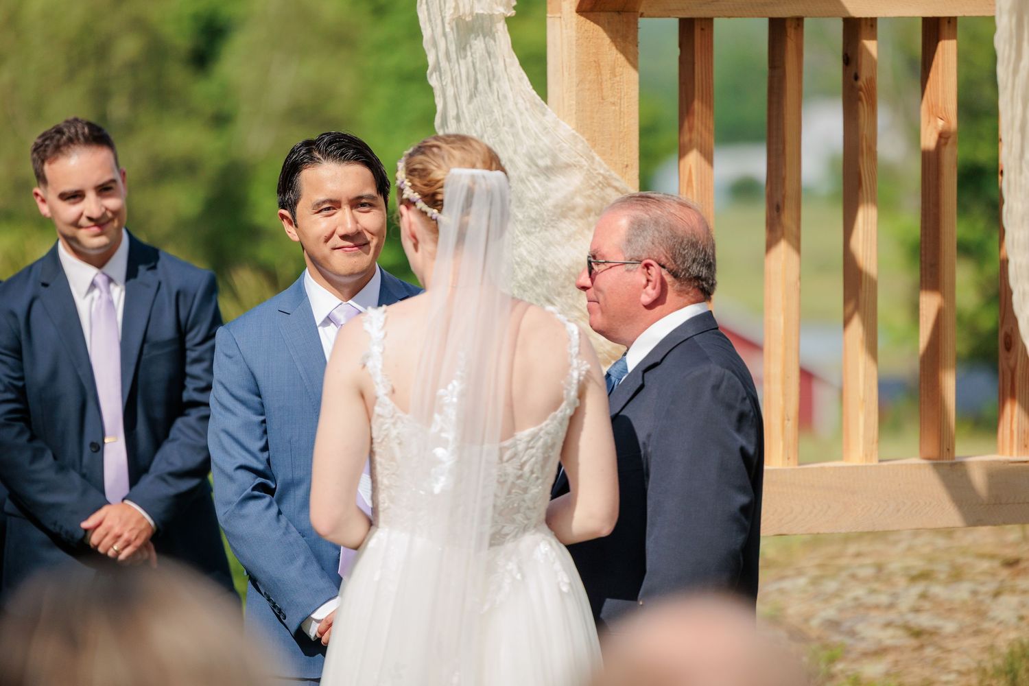 Father presenting bride to groom at outdoor wedding ceremony altar with wooden arch and wedding party.