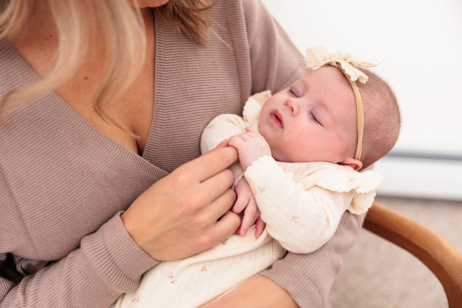 Baby in cream outfit resting peacefully while being cradled and fed in caregiver's arms.