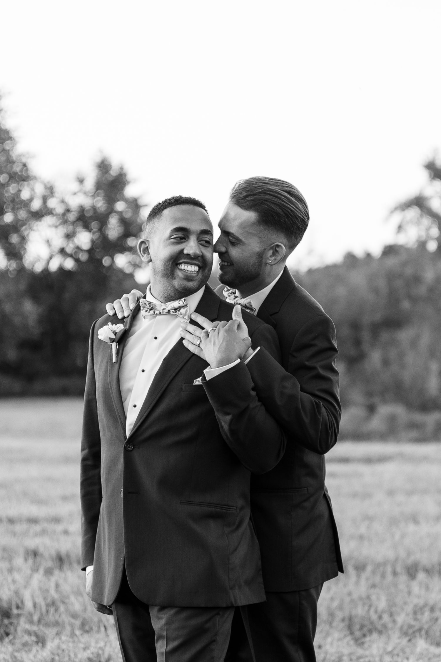 Black and white photo of two people in formal attire sharing tender moment outdoors.