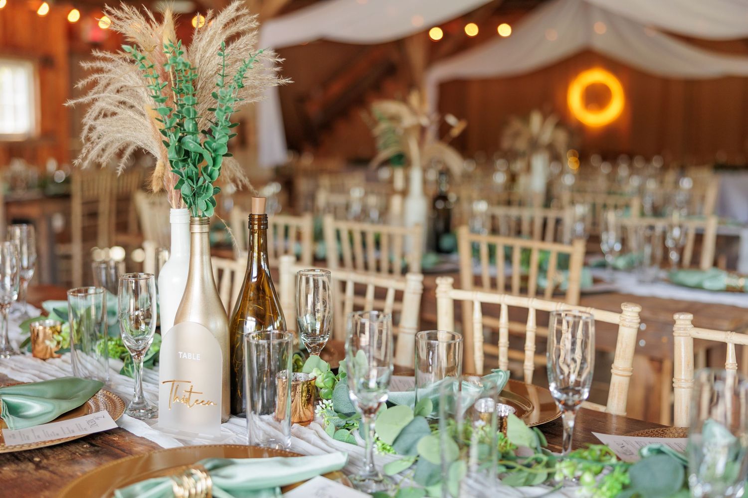 Wedding reception tables decorated with sage green accents, white linens, and gold chairs.