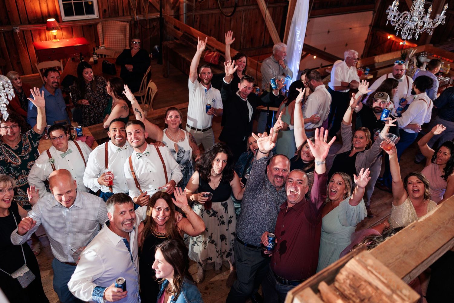 Large group of wedding guests dancing and celebrating inside a rustic barn venue.