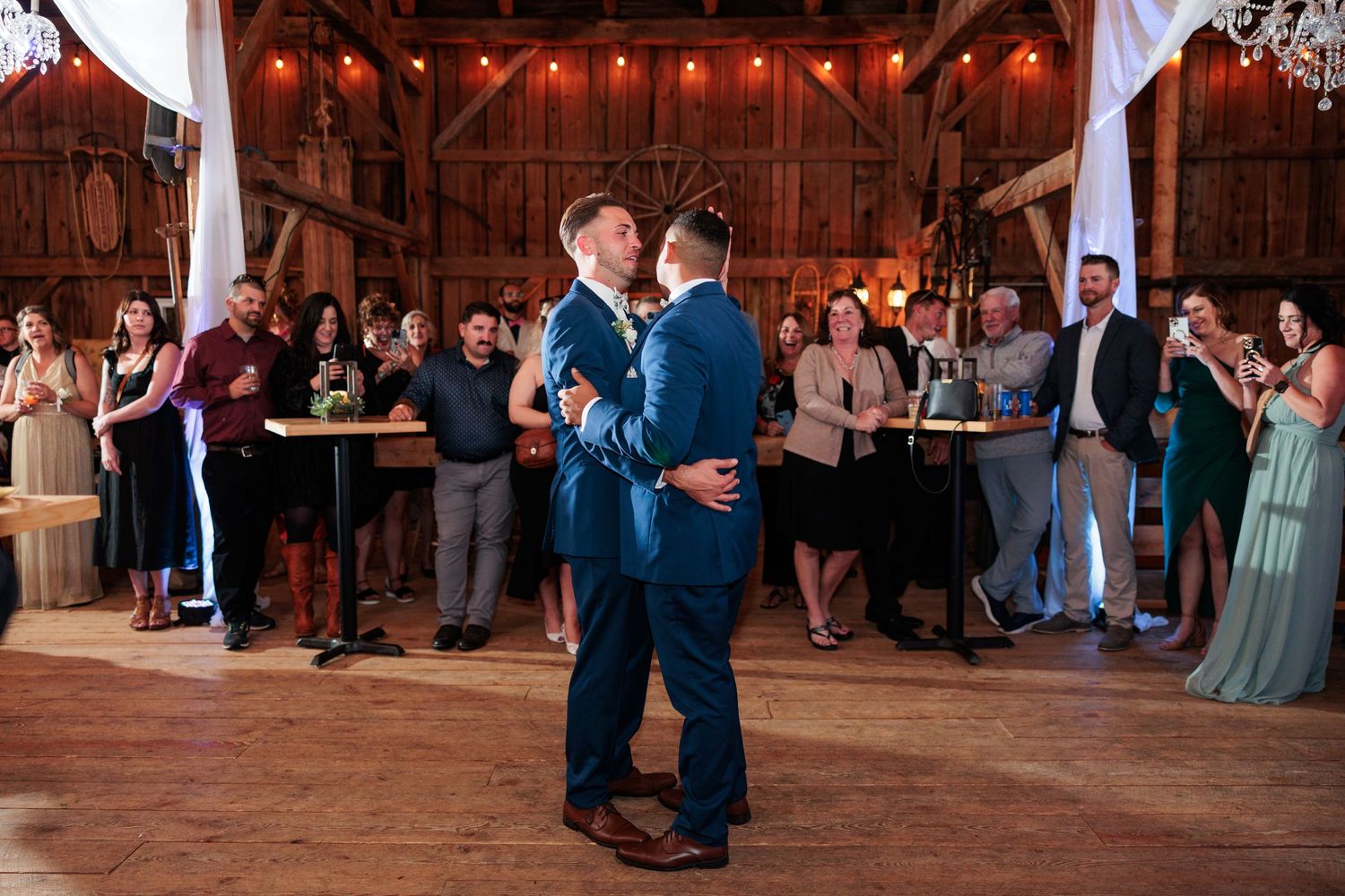 Couples dance together in a rustic barn venue decorated with string lights.
