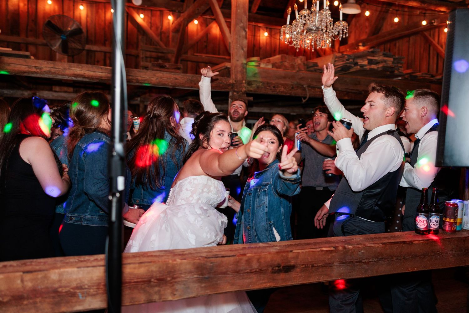 Energetic wedding reception scene with guests dancing and celebrating under chandeliers.