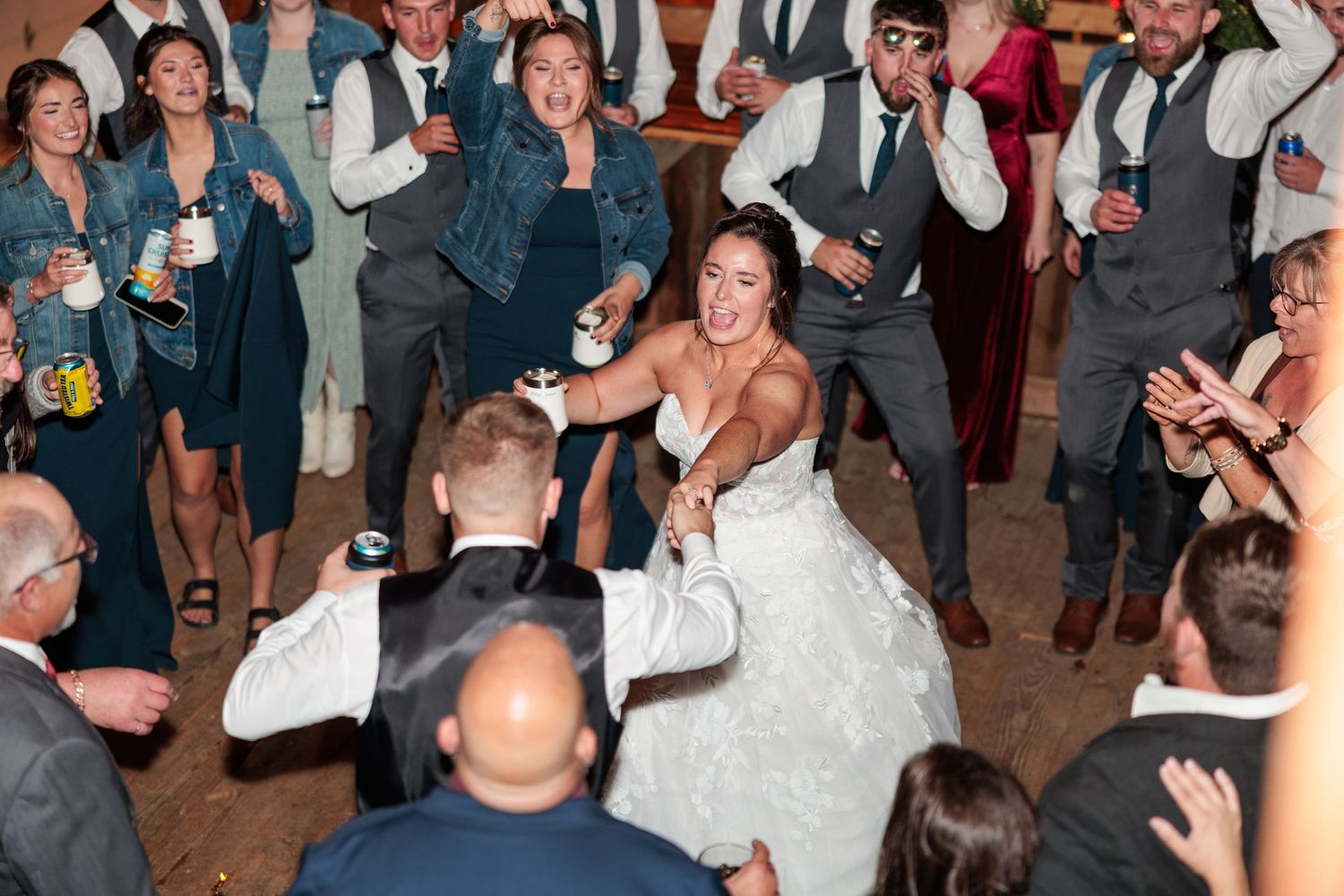 Bride laughs joyfully on the dance floor surrounded by cheering wedding guests at a lively reception.