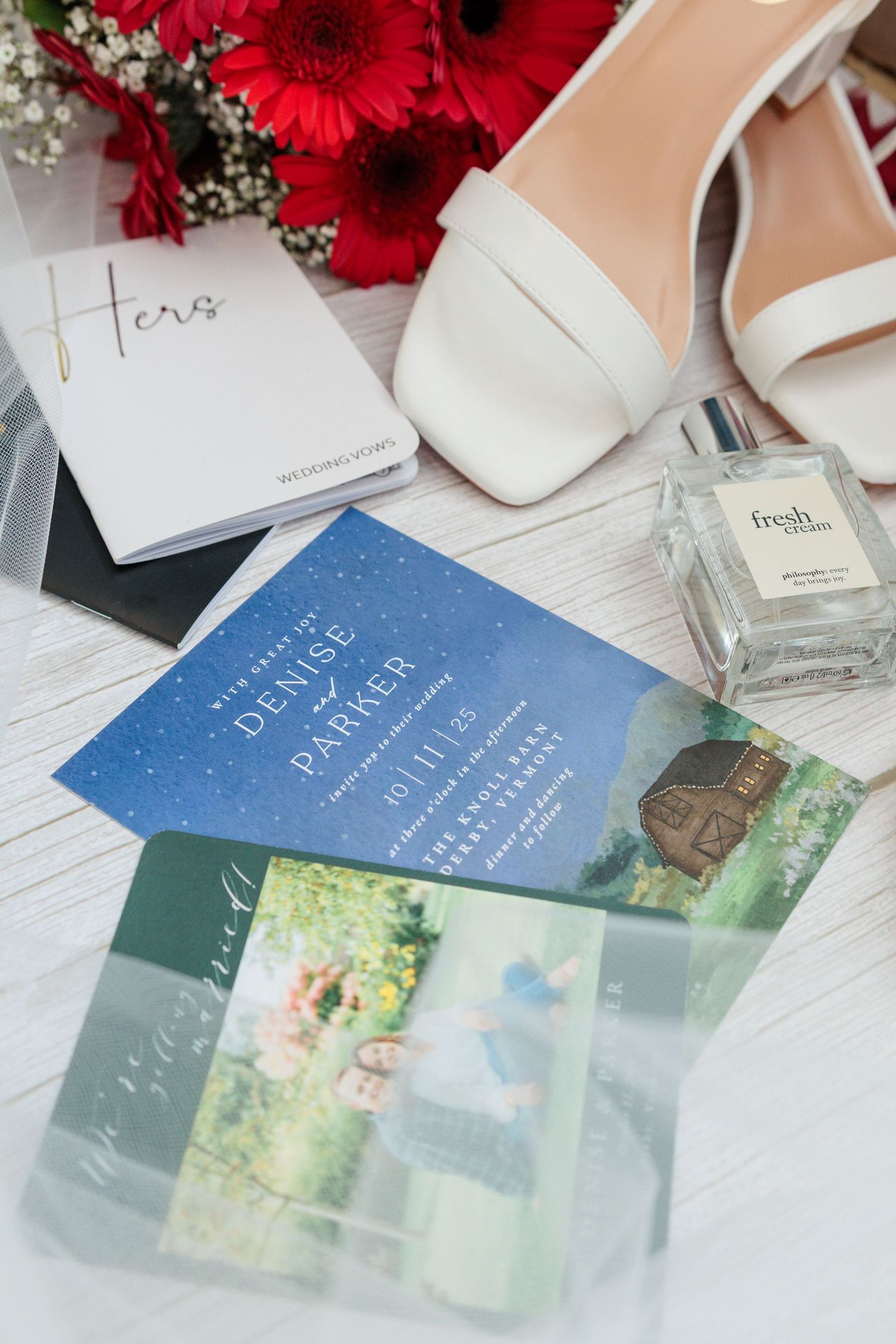 Wedding flat lay featuring blue starry invitation for Denise and Parker, white heels, perfume, and red flowers.