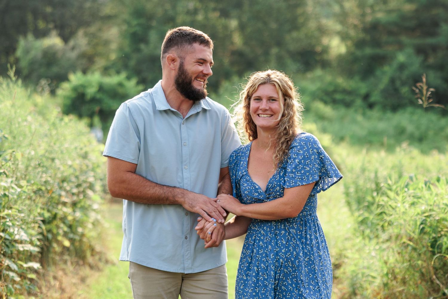 Happy couple holding hands and smiling together on a scenic green garden path in summer.