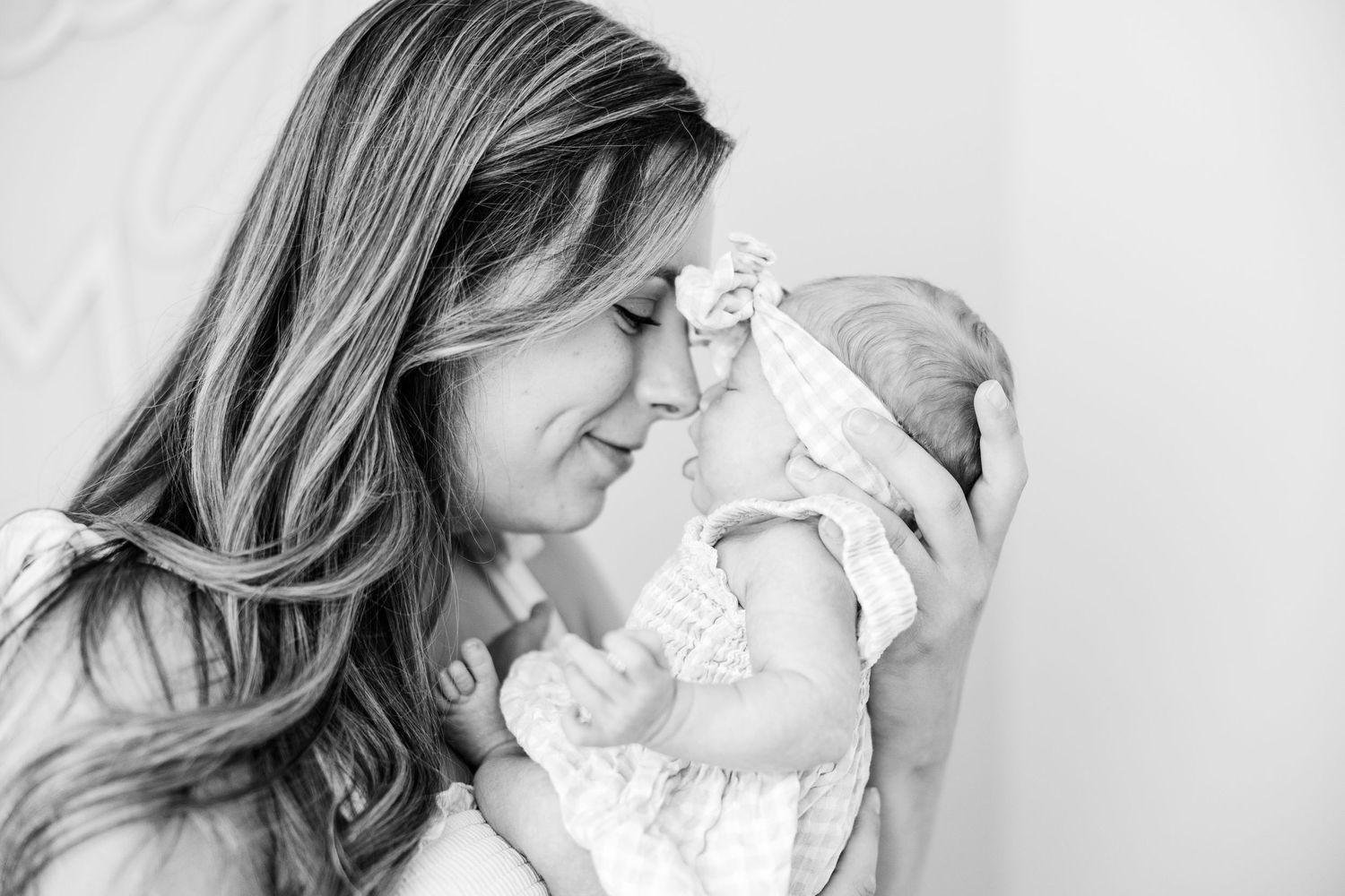 Tender black and white portrait of a mother touching foreheads with her newborn baby.