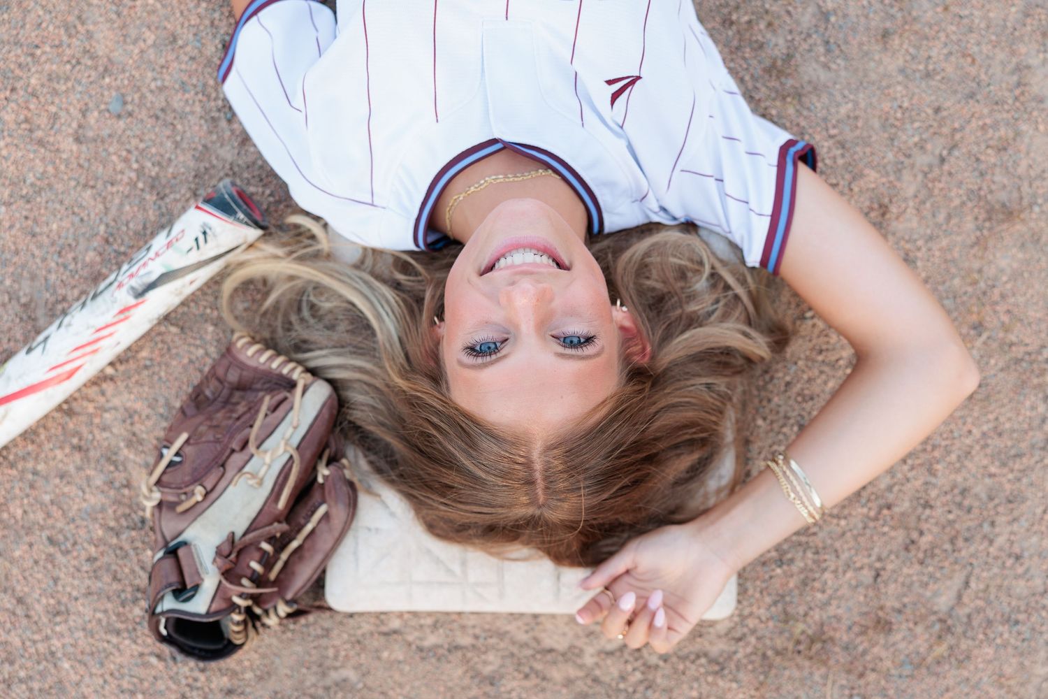 Young female softball player lying on ground with baseball glove, wearing white jersey, hair spread out.