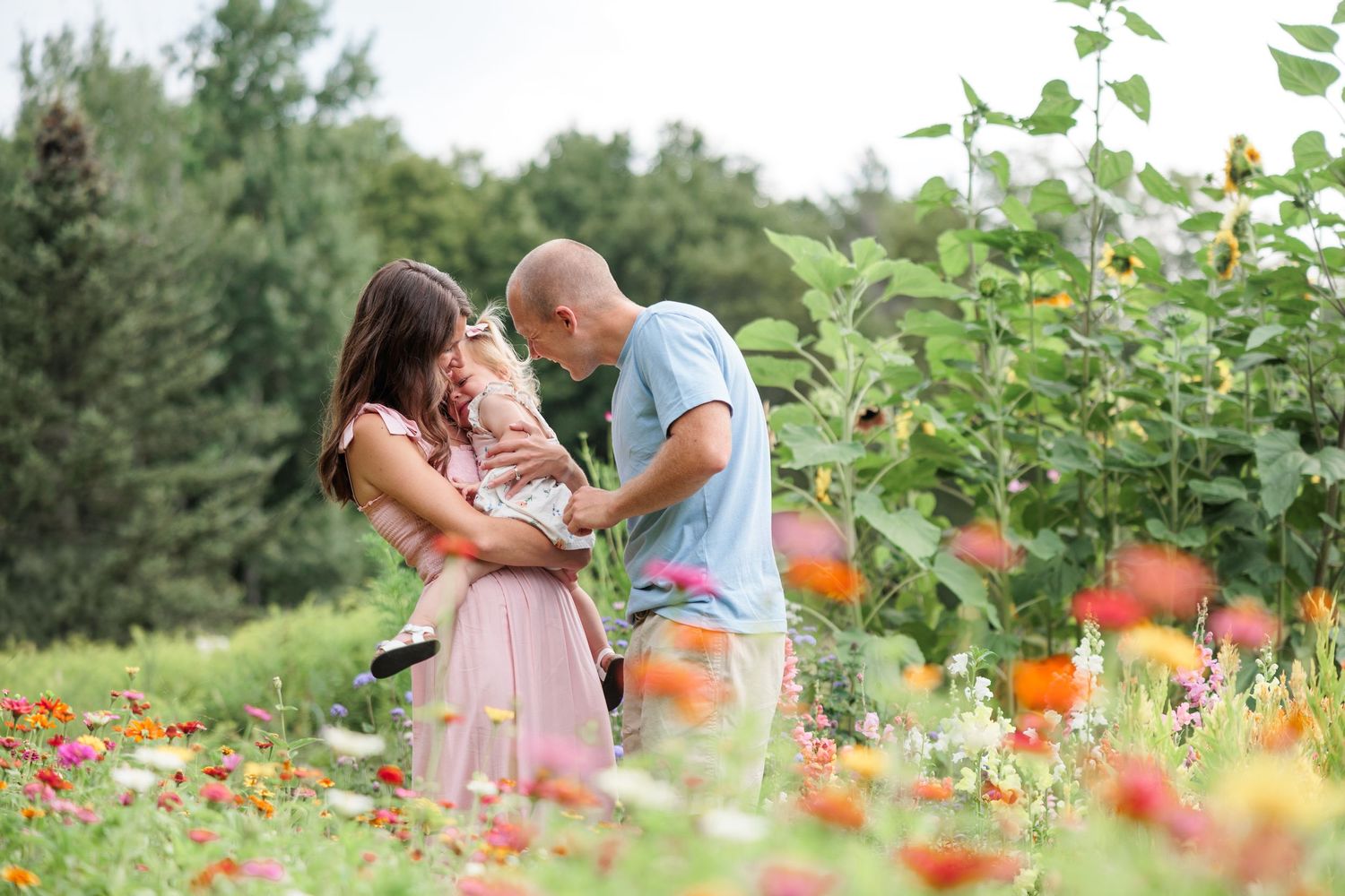 A couple lovingly holds their baby together in a vibrant garden filled with colorful flowers.