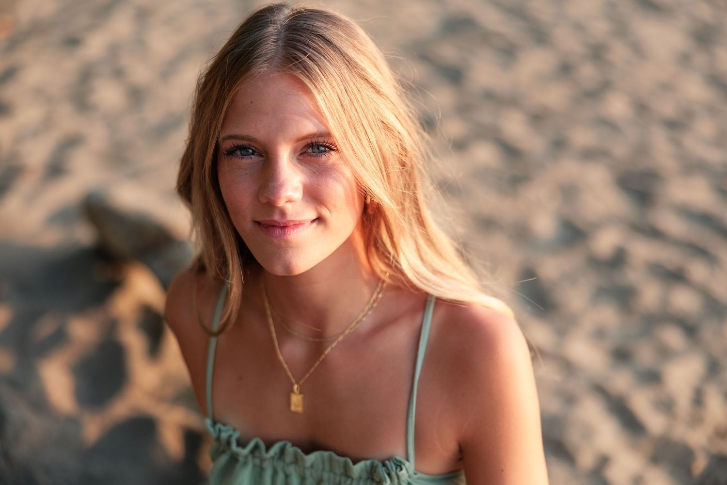 Young blonde woman smiling at camera on sandy beach at golden hour.