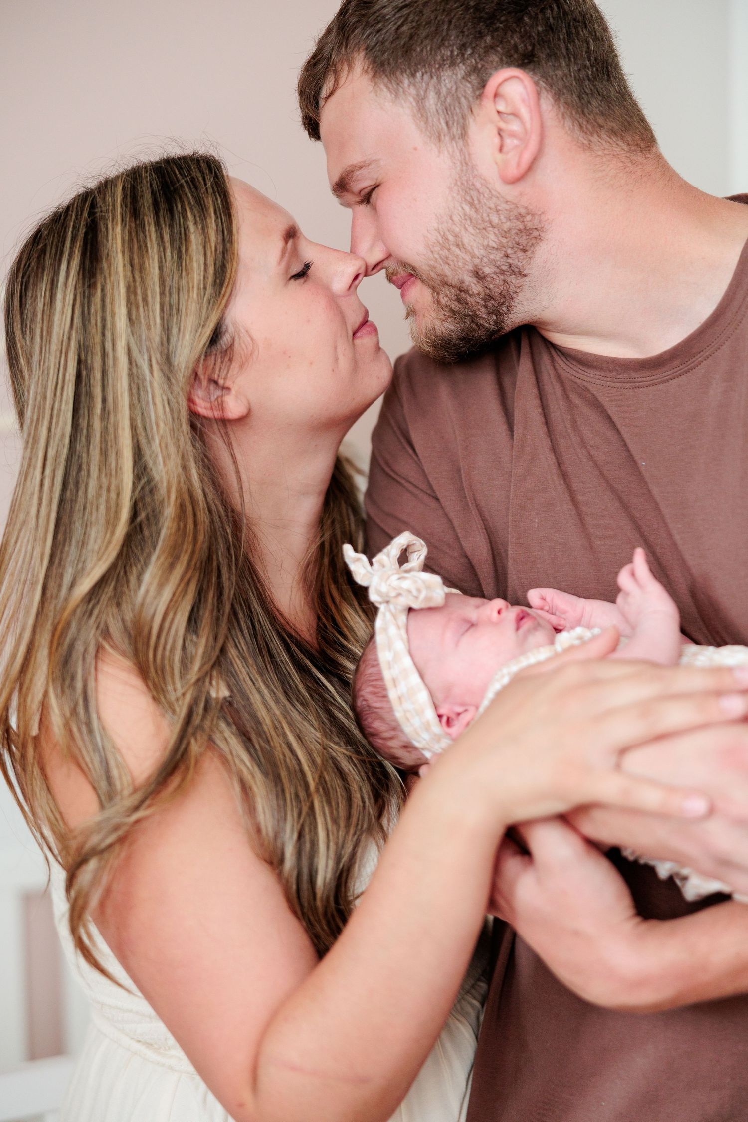 New parents share a tender kiss while holding their swaddled newborn baby together.