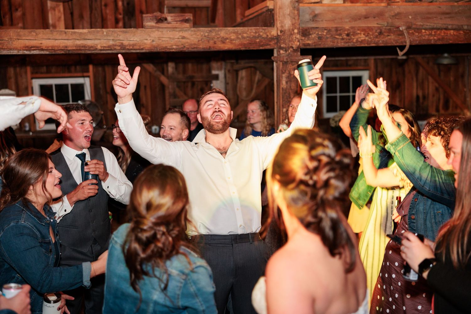 Excited wedding guest celebrates with arms raised on the dance floor at a lively barn reception.