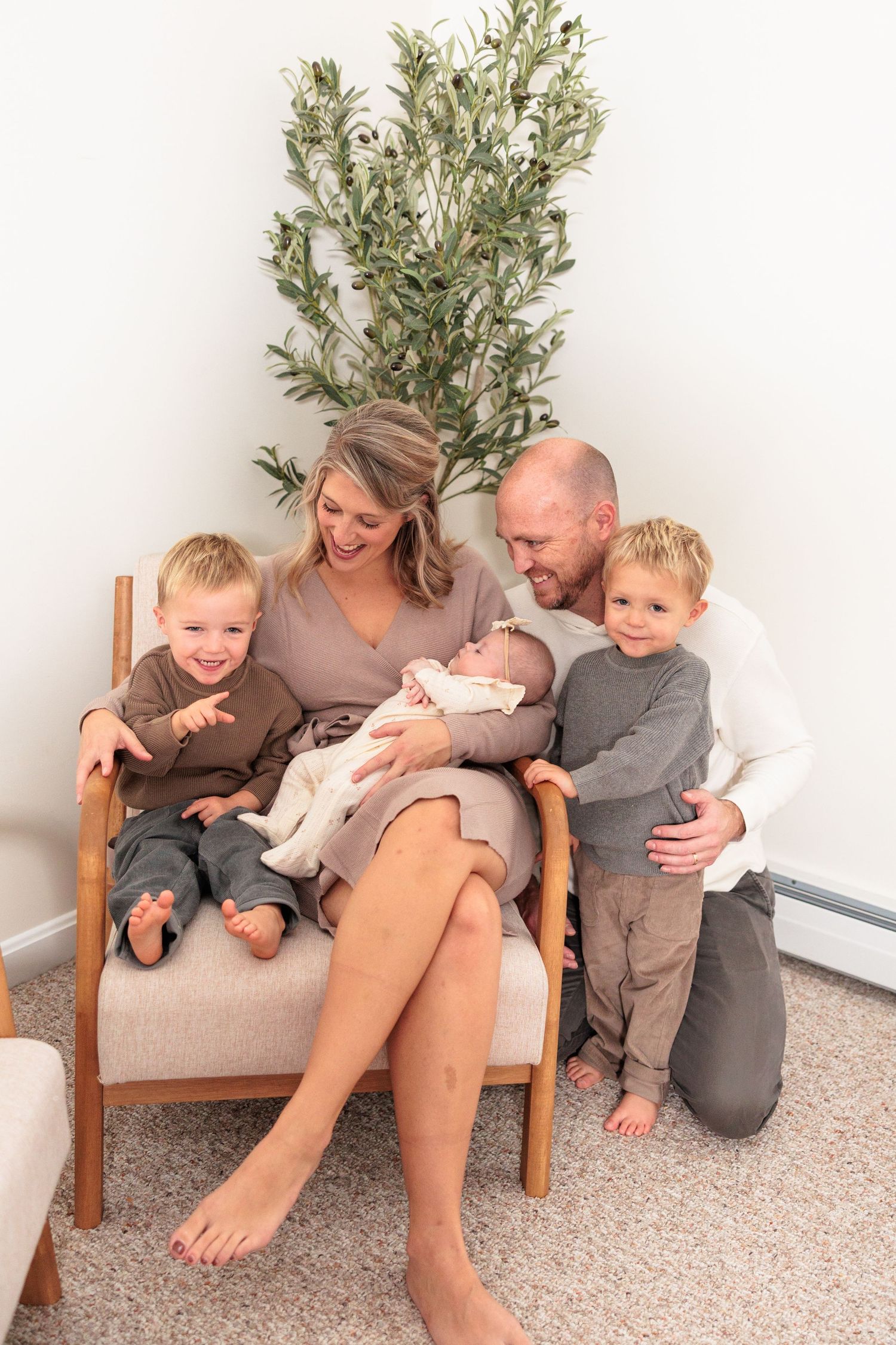 A family sits together on a beige chair with a green plant in the background, sharing a tender moment at home.
