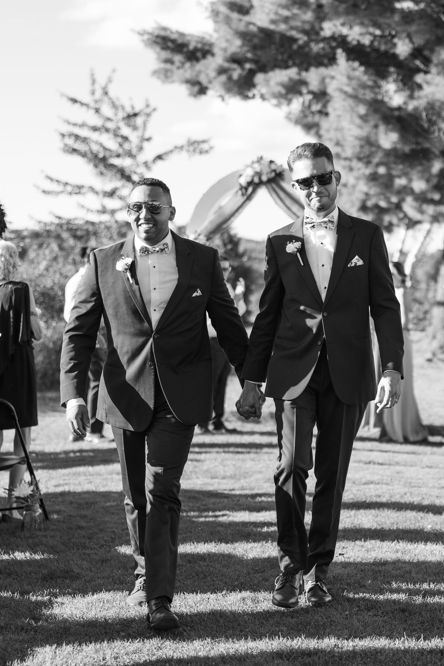 Wedding party members in navy suits walk across a grassy lawn during an outdoor celebration.
