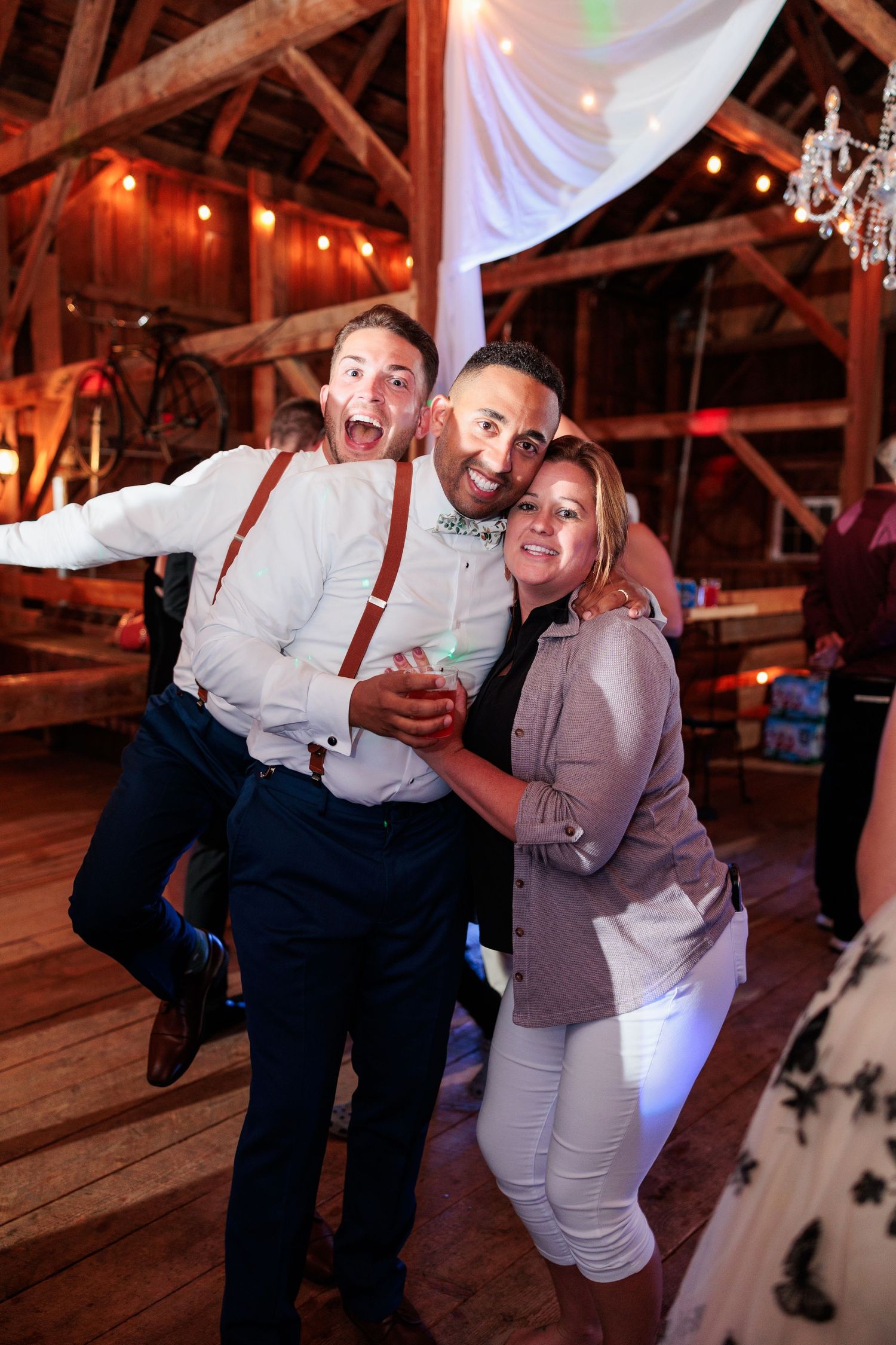 Party guests celebrating inside a rustic barn venue with chandelier and wooden beams.