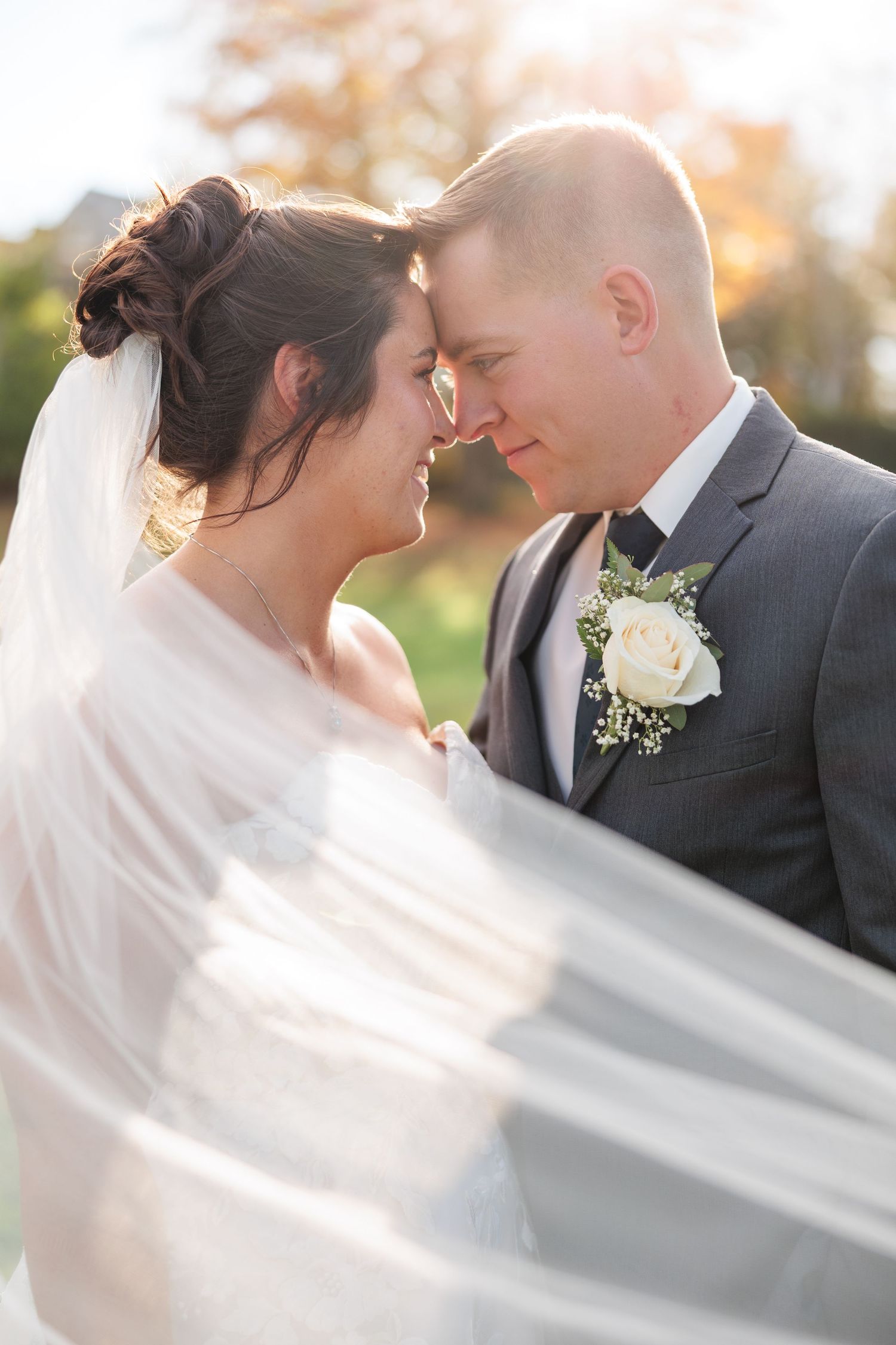 Romantic wedding portrait with flowing veil captured in soft sunlight.