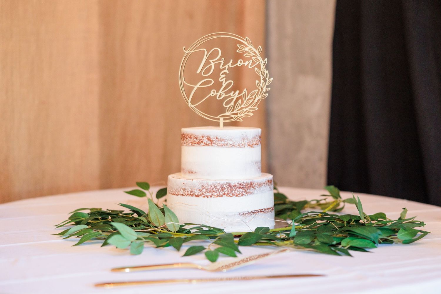 Elegant wedding cake display with white frosting and greenery accents on a rustic wooden table.