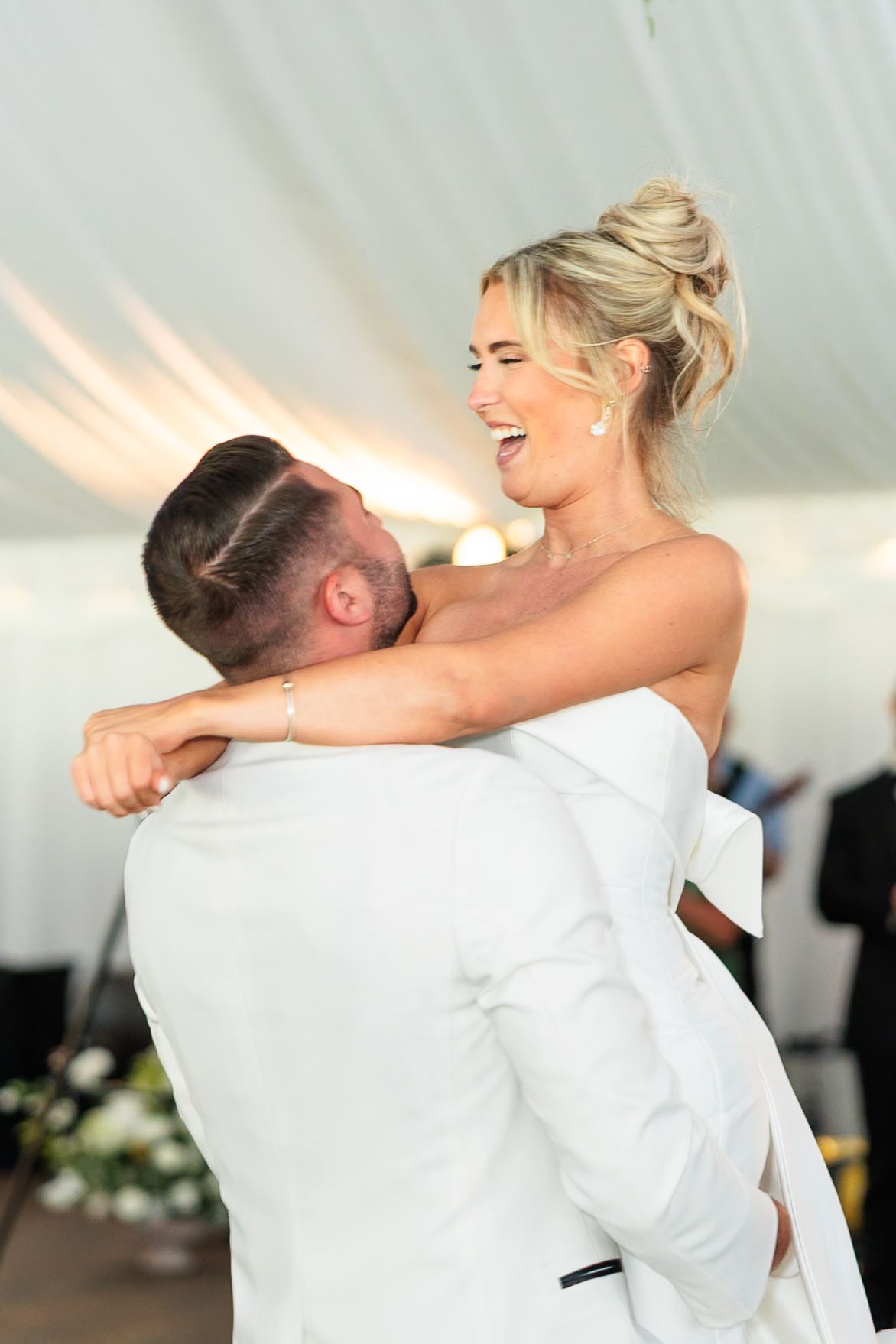 Groom lifts laughing bride during joyful first dance at elegant tented wedding reception.