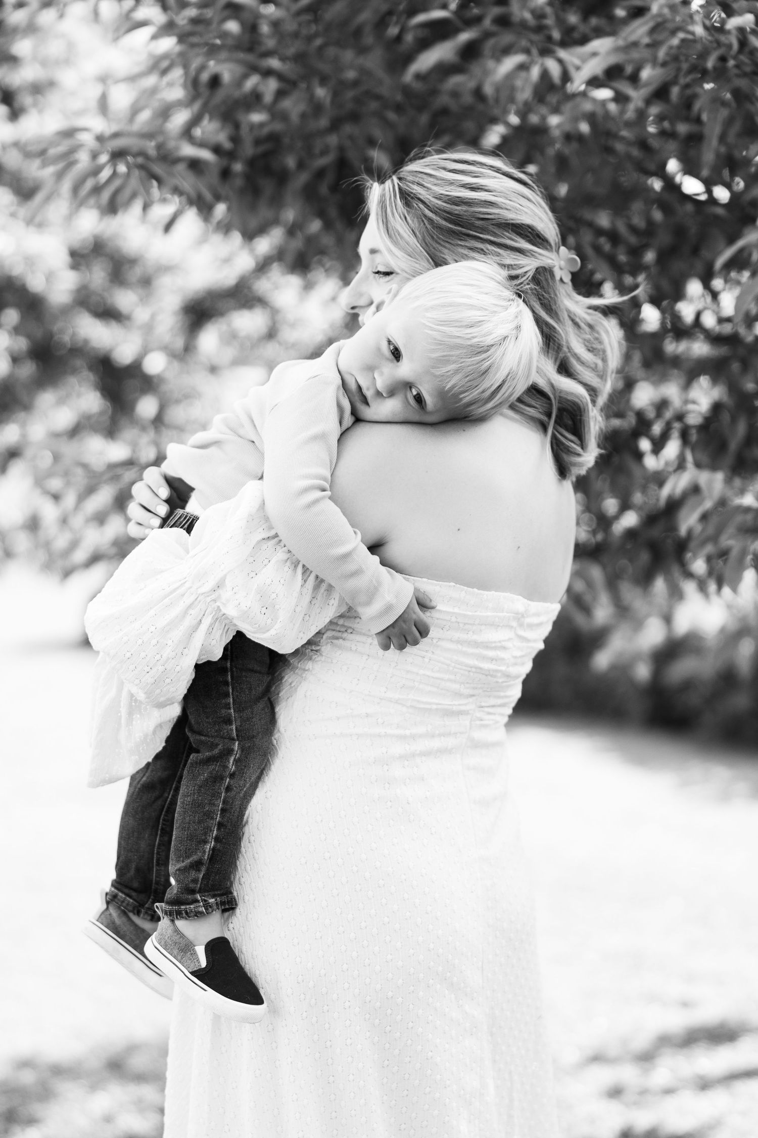 Black and white photo of a pregnant woman in white dress holding a young child outdoors.
