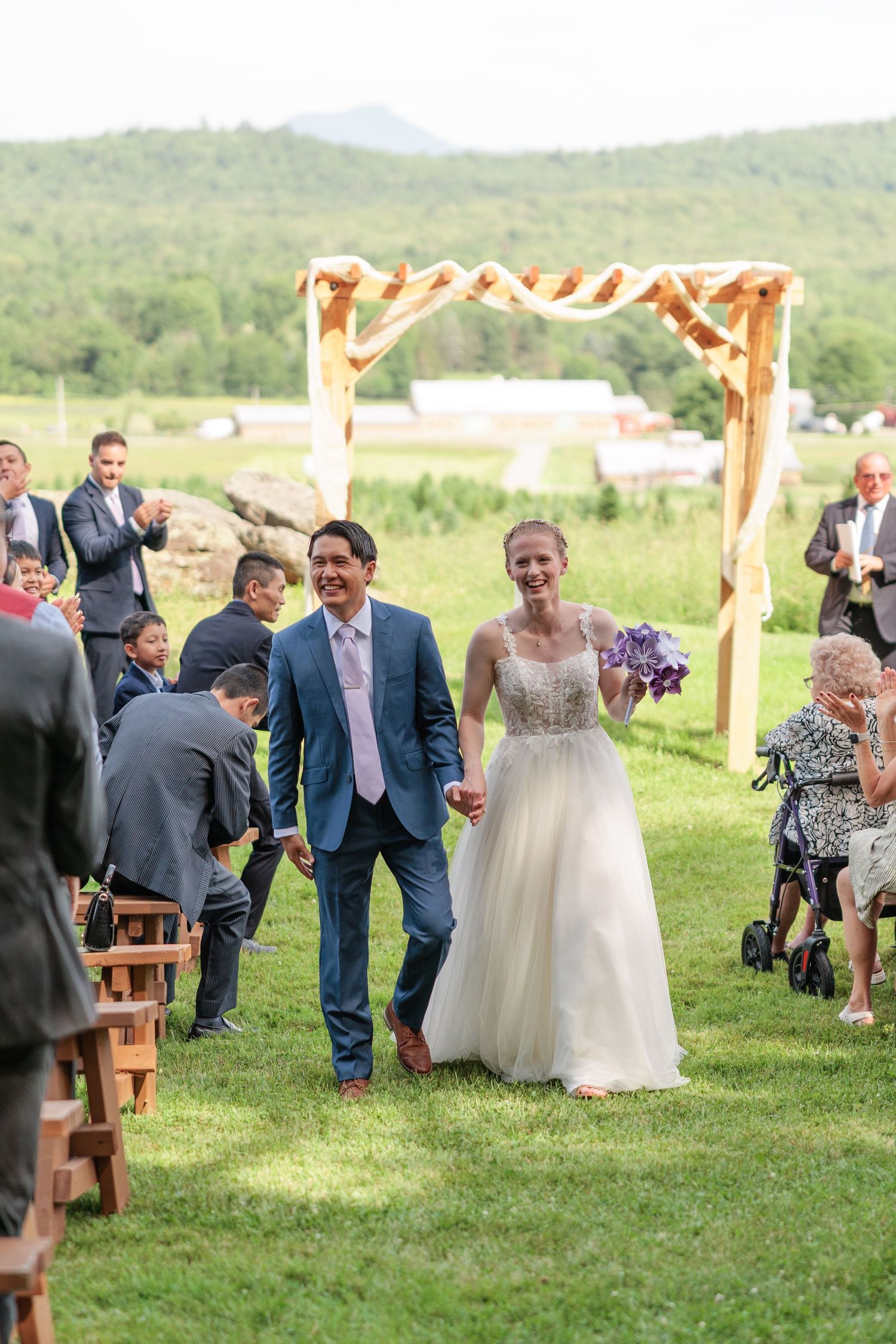 Joyful newlyweds walking back down the aisle after ceremony under a wooden arch with mountain backdrop.
