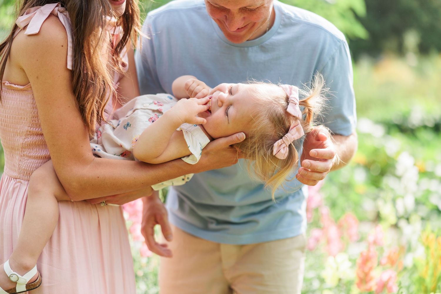 Happy family with parents holding a laughing baby girl outdoors in a blooming garden.