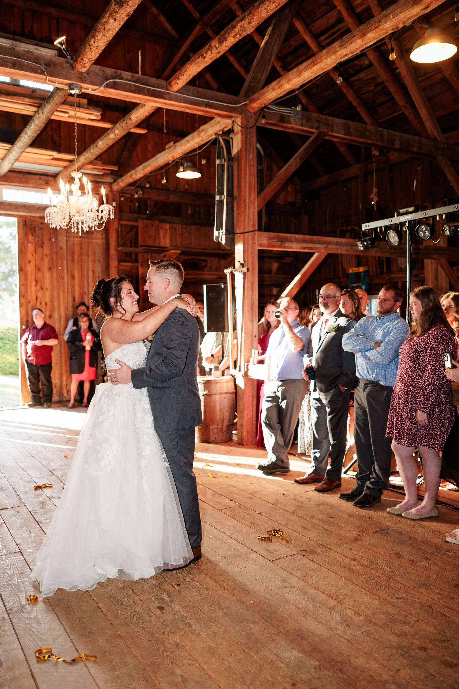 Wedding couple's first dance in rustic wooden barn venue with guests watching.