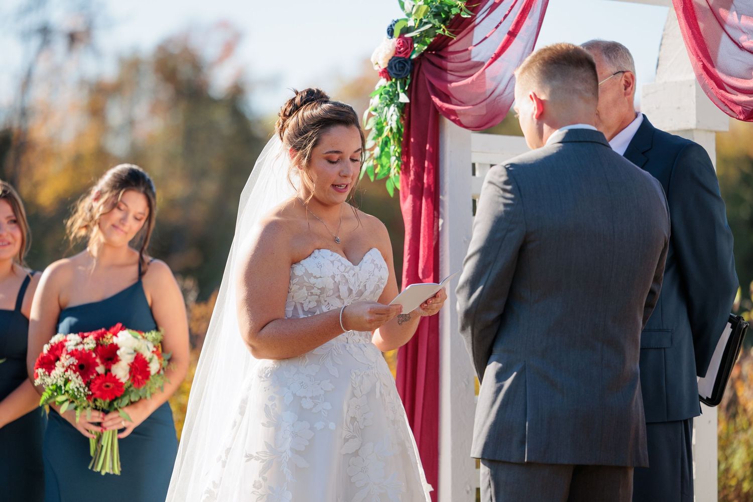 Wedding ceremony setup with burgundy drapes and floral arrangements under sunny autumn skies.