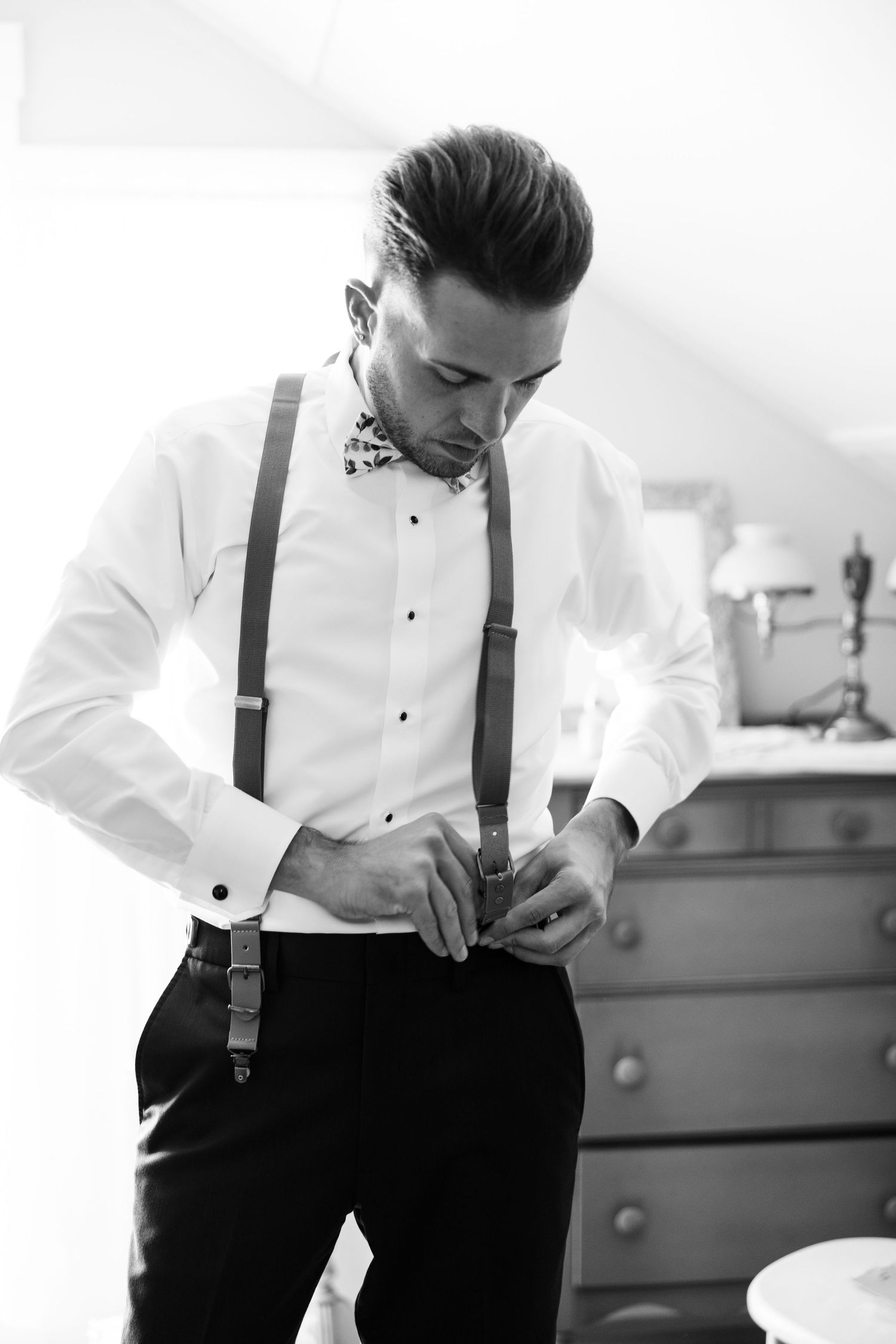 Groom adjusting his suspenders while getting ready in black and white.