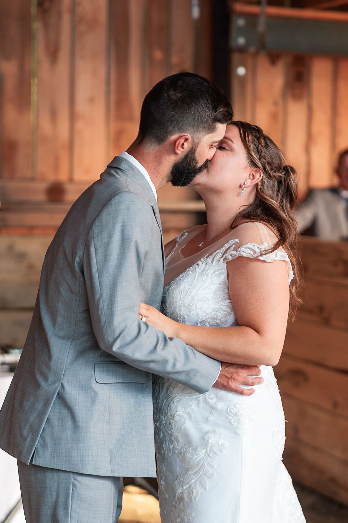 Bride and groom share a romantic kiss during their first dance in a warm wooden barn reception hall.