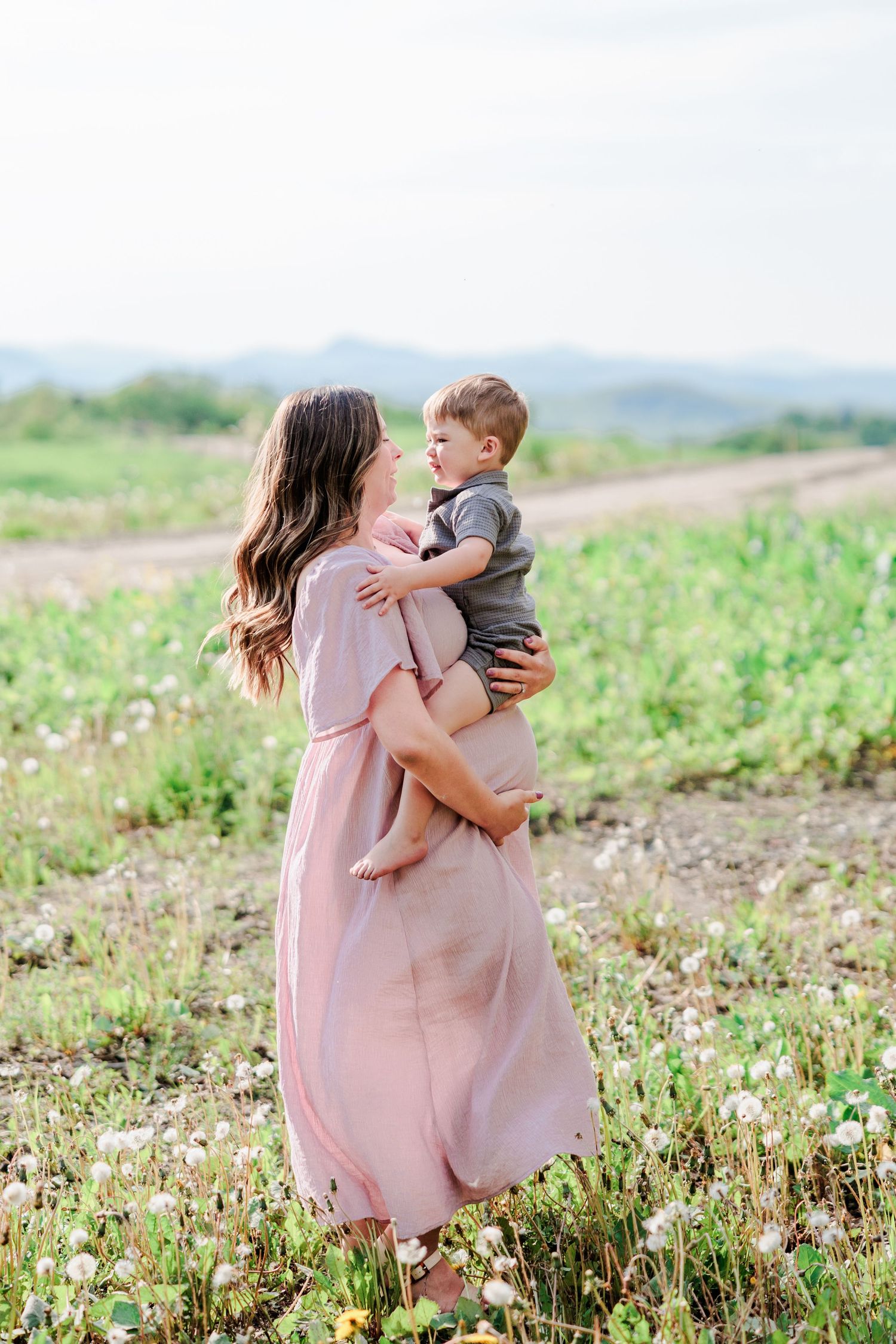 Mother in pink dress holding her toddler son in a flower-filled meadow.