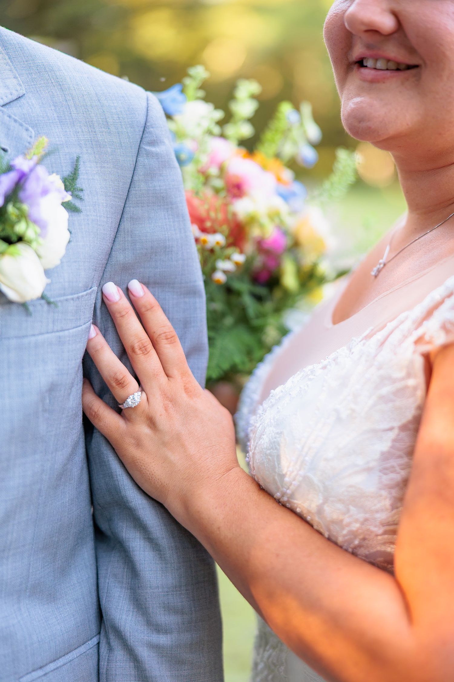 Close-up of bride's hand with diamond engagement ring resting on groom's gray suit jacket at wedding.