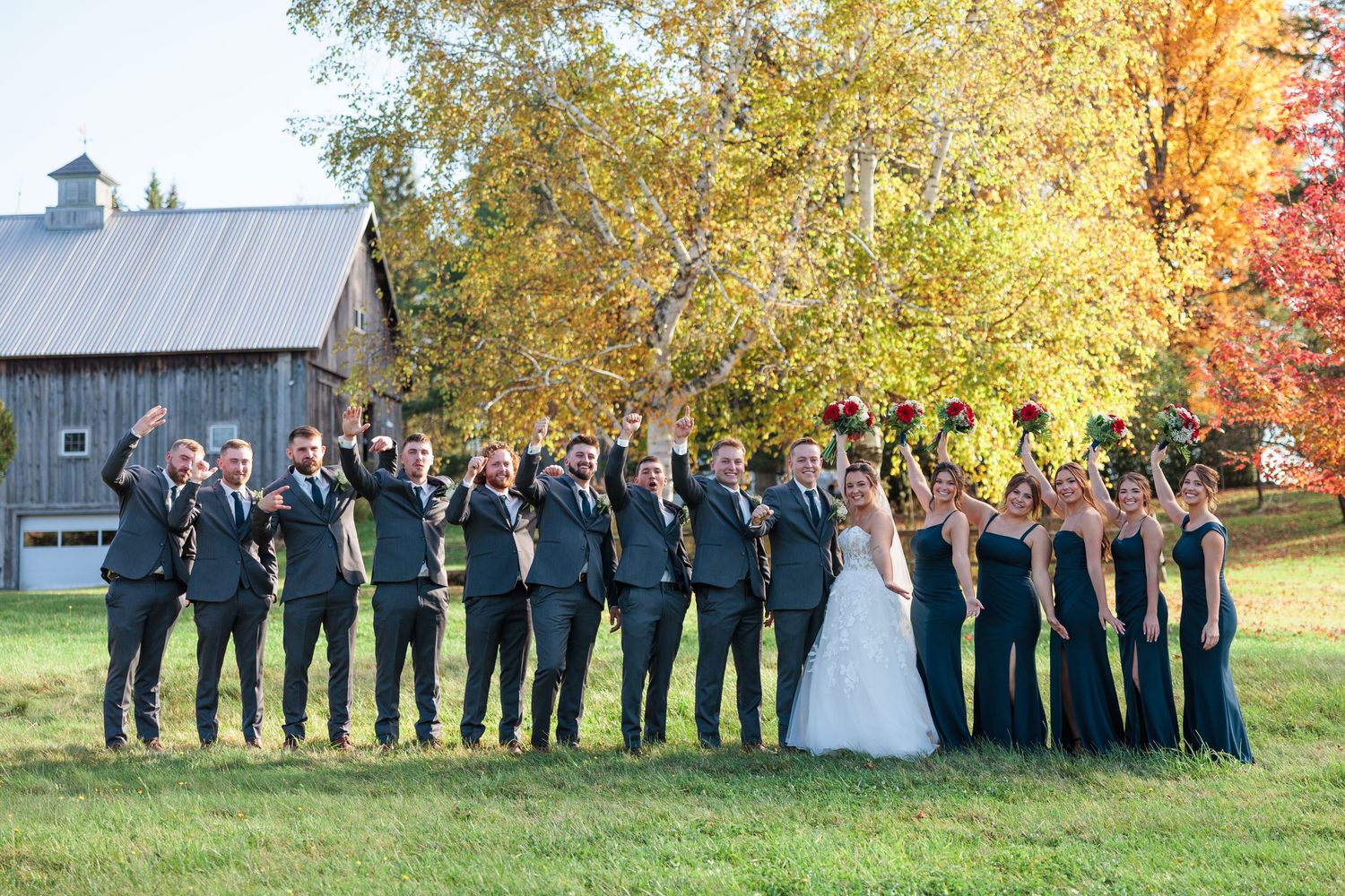 Large wedding party lined up for photo with navy attire against autumn landscape.