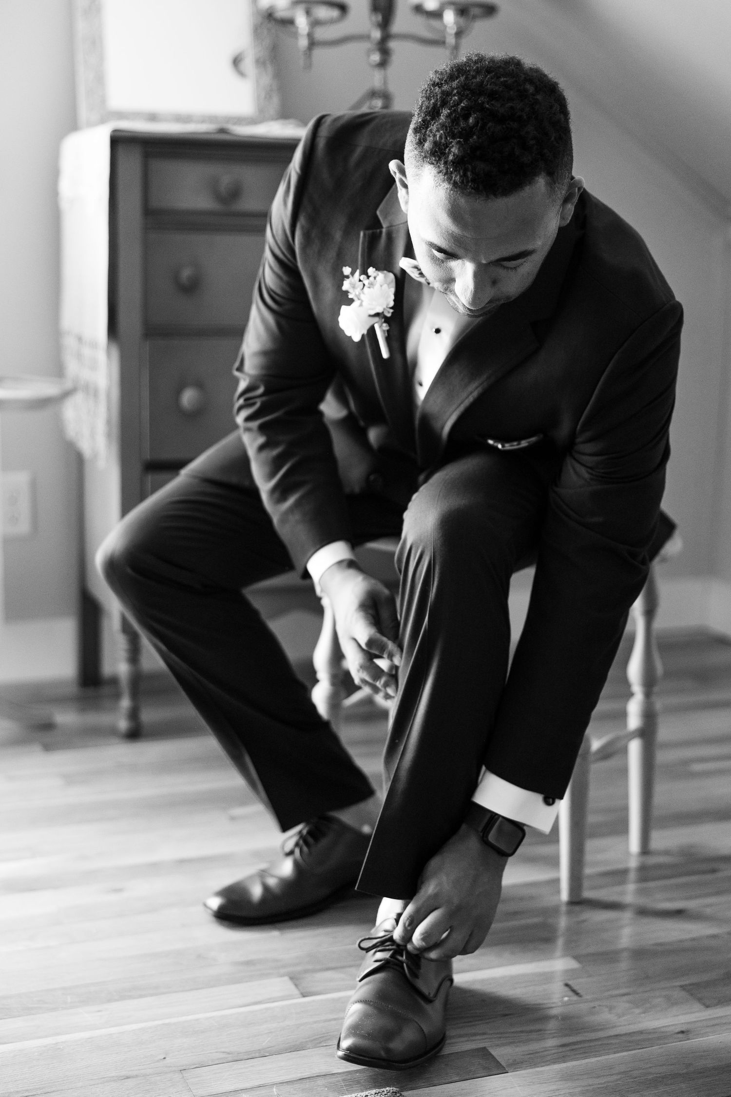 Black and white shot of groom adjusting his shoes before ceremony.