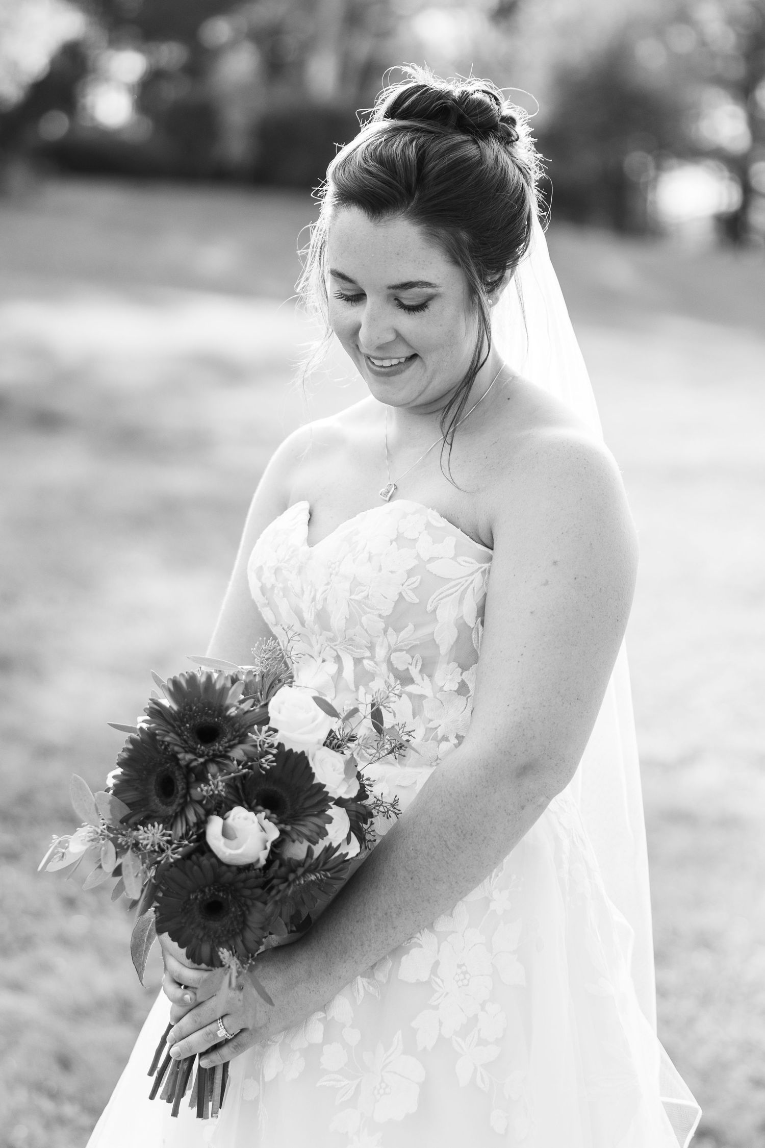 Elegant bride in white lace gown holds a vibrant bouquet featuring sunflowers and mixed blooms outdoors.