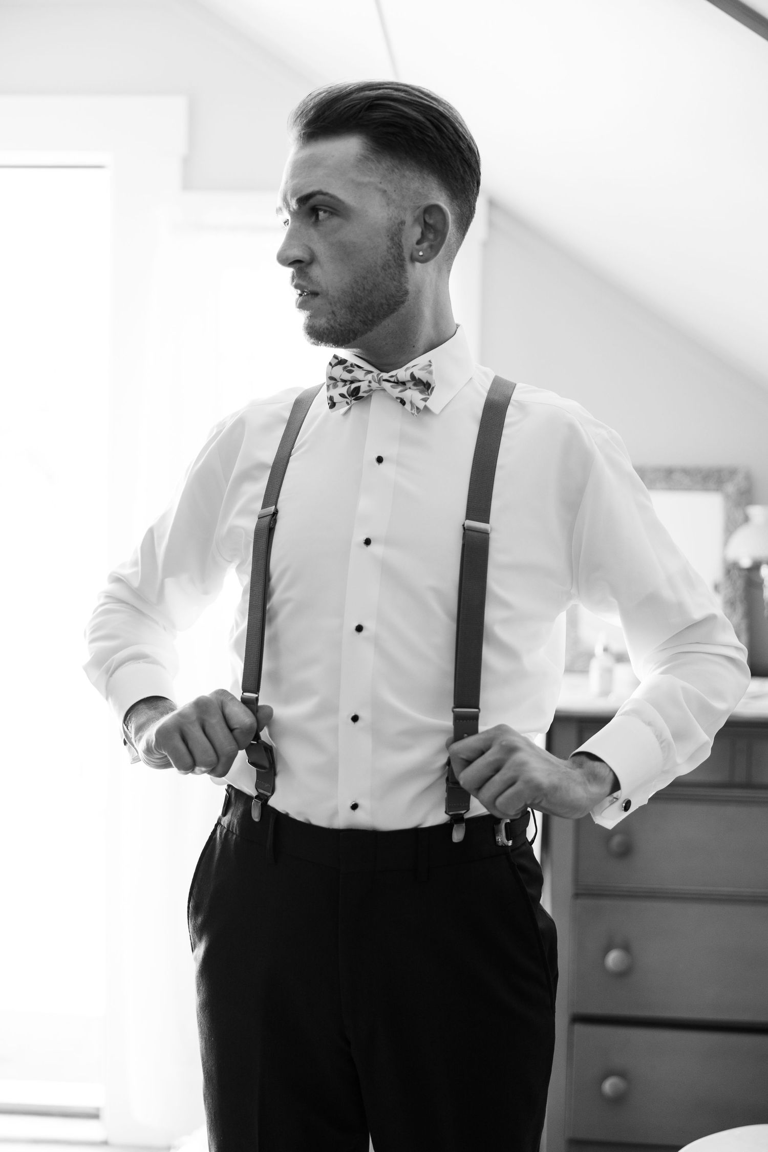 Stylish groom in white shirt and bow tie with suspenders preparing for wedding.