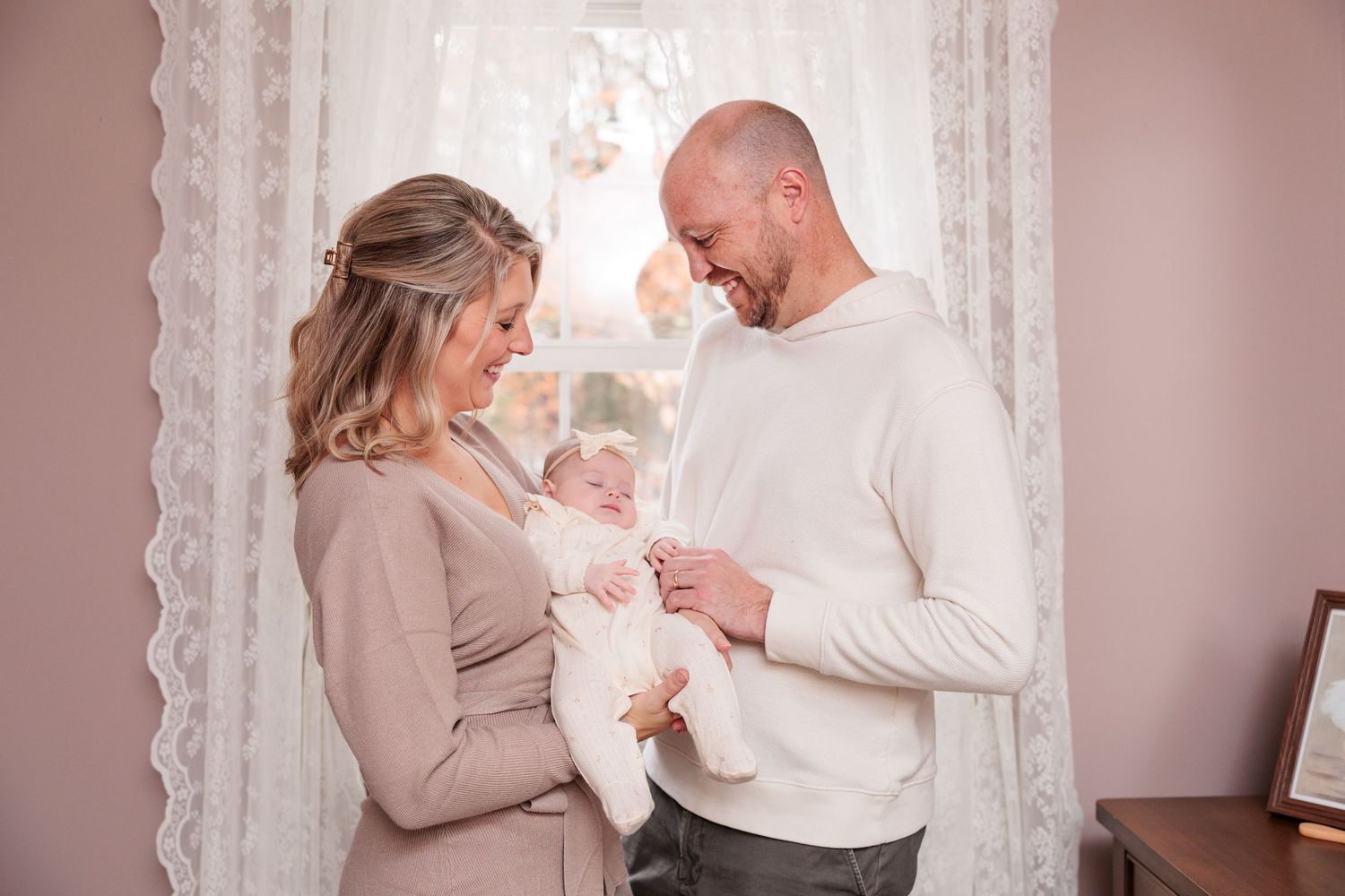 Intimate family portrait session showing tender moments in a softly lit room with lace curtains.