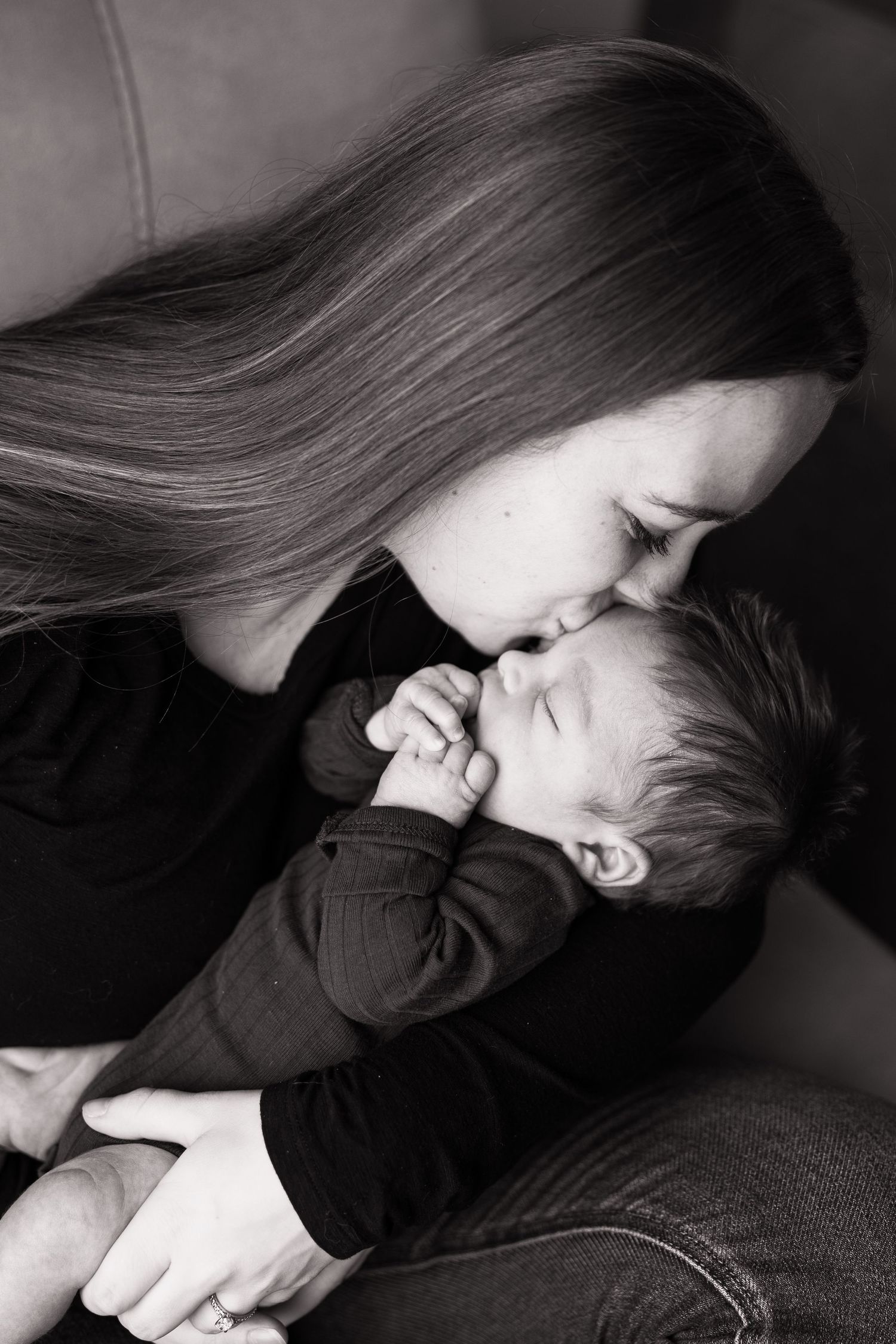 Black and white photo of a mother tenderly kissing her sleeping newborn baby.