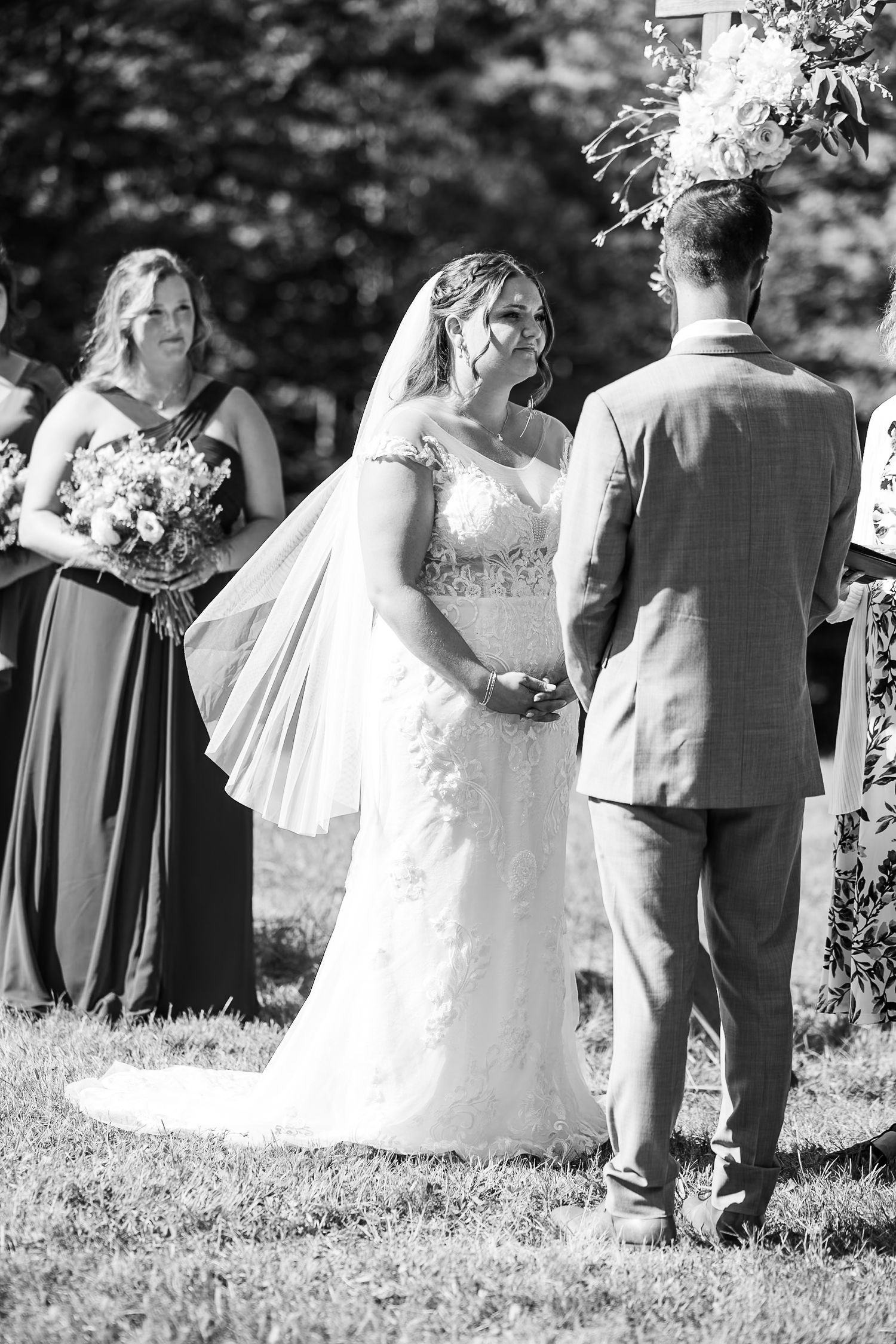 Emotional bride laughs joyfully while exchanging vows with groom at sunny outdoor wedding ceremony.