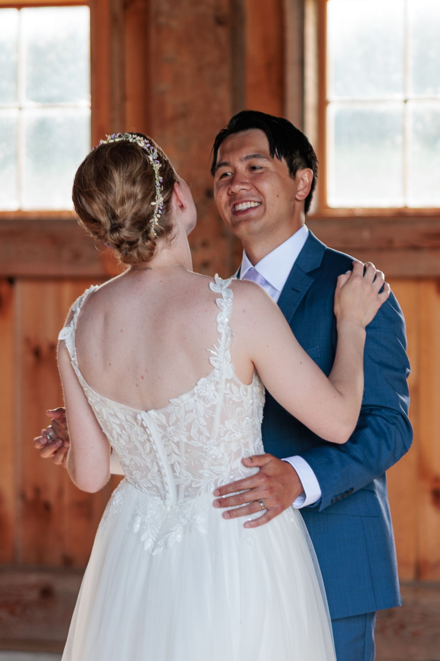 Bride and groom share their first dance, smiling at each other in a rustic barn wedding venue.