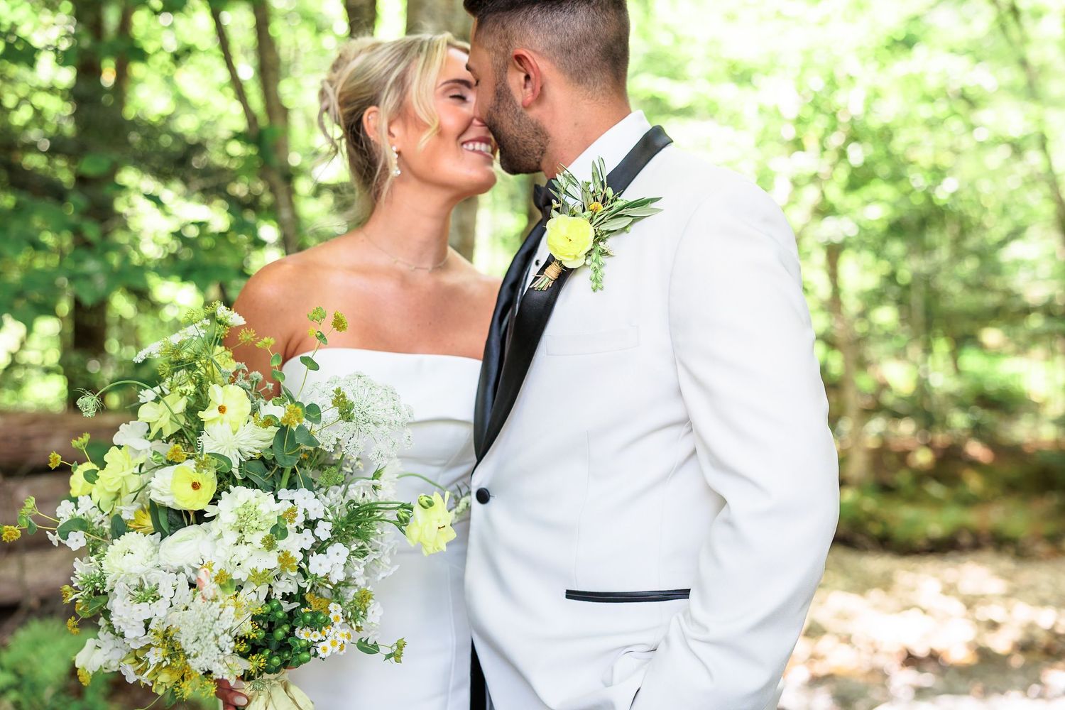 Smiling bride and groom sharing a romantic moment in a sunlit forest on their wedding day.